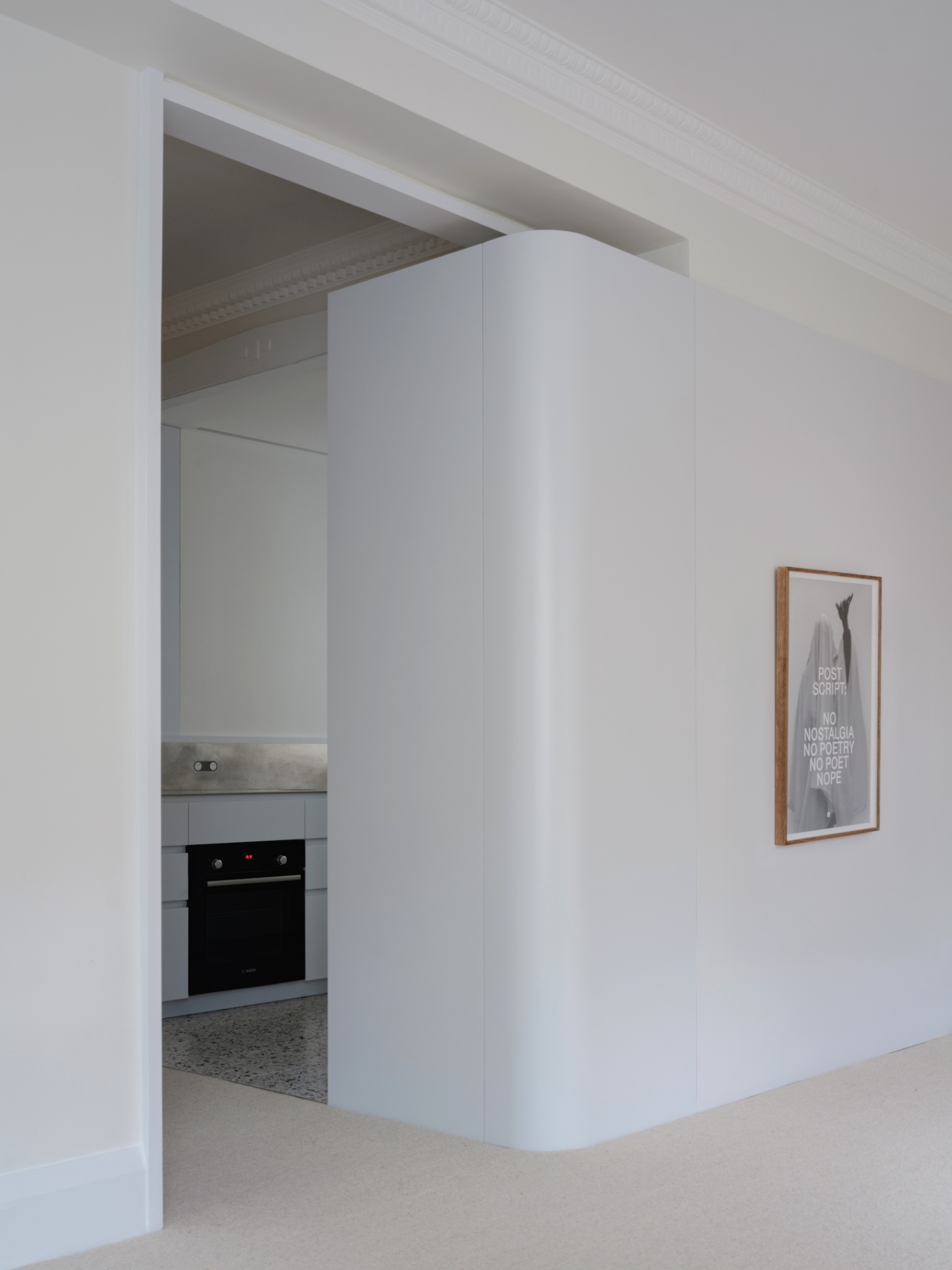 Onslow Gardens Apartment by Youssofzay Hart — A white curved volume anchors the threshold between living and kitchen spaces, its cylindrical form creating a sculptural passage element.