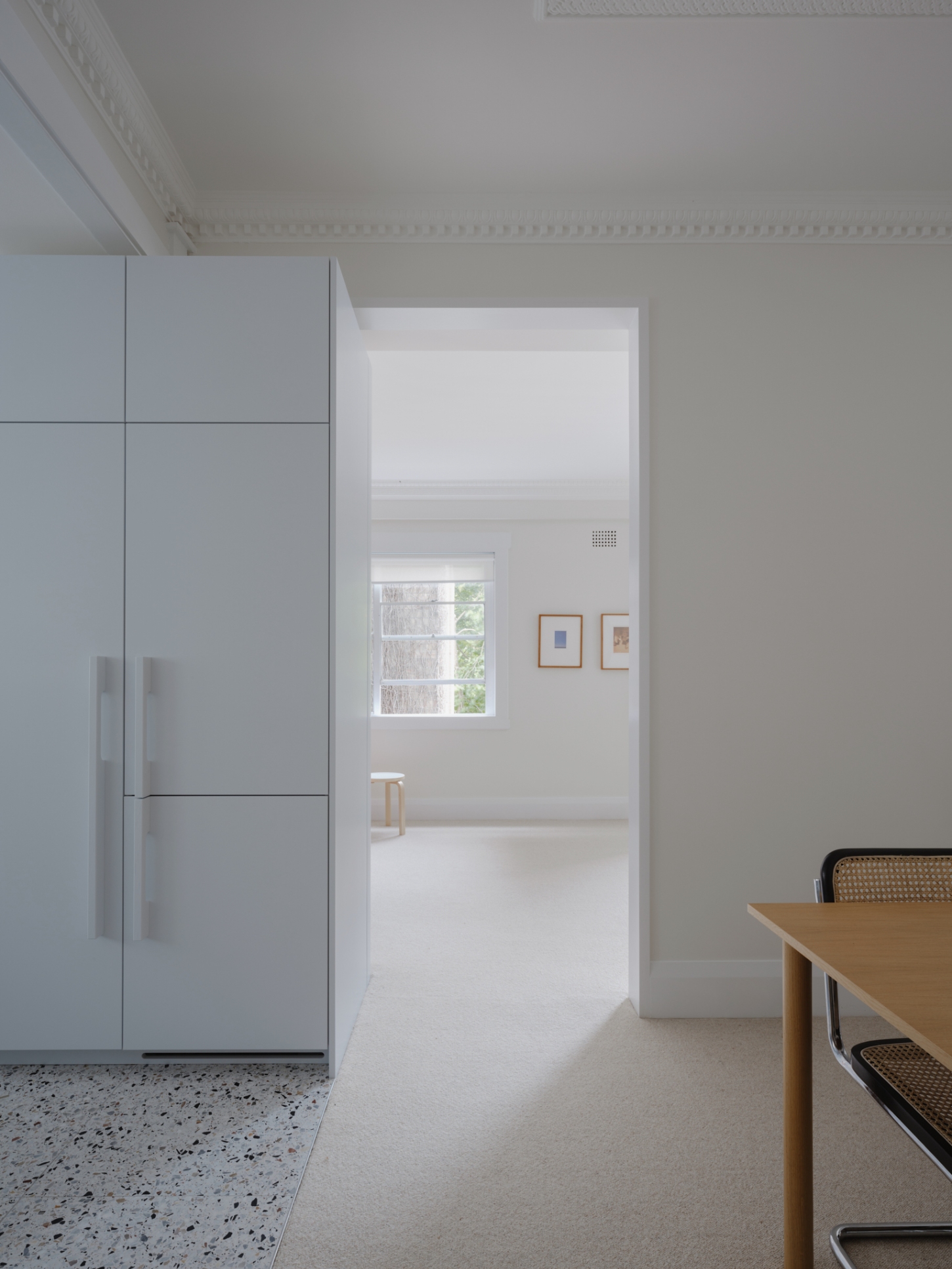 Onslow Gardens Apartment by Youssofzay Hart — The kitchen threshold frames a clean sightline through to the living space beyond, where natural light streams across white flooring in continuous planes.