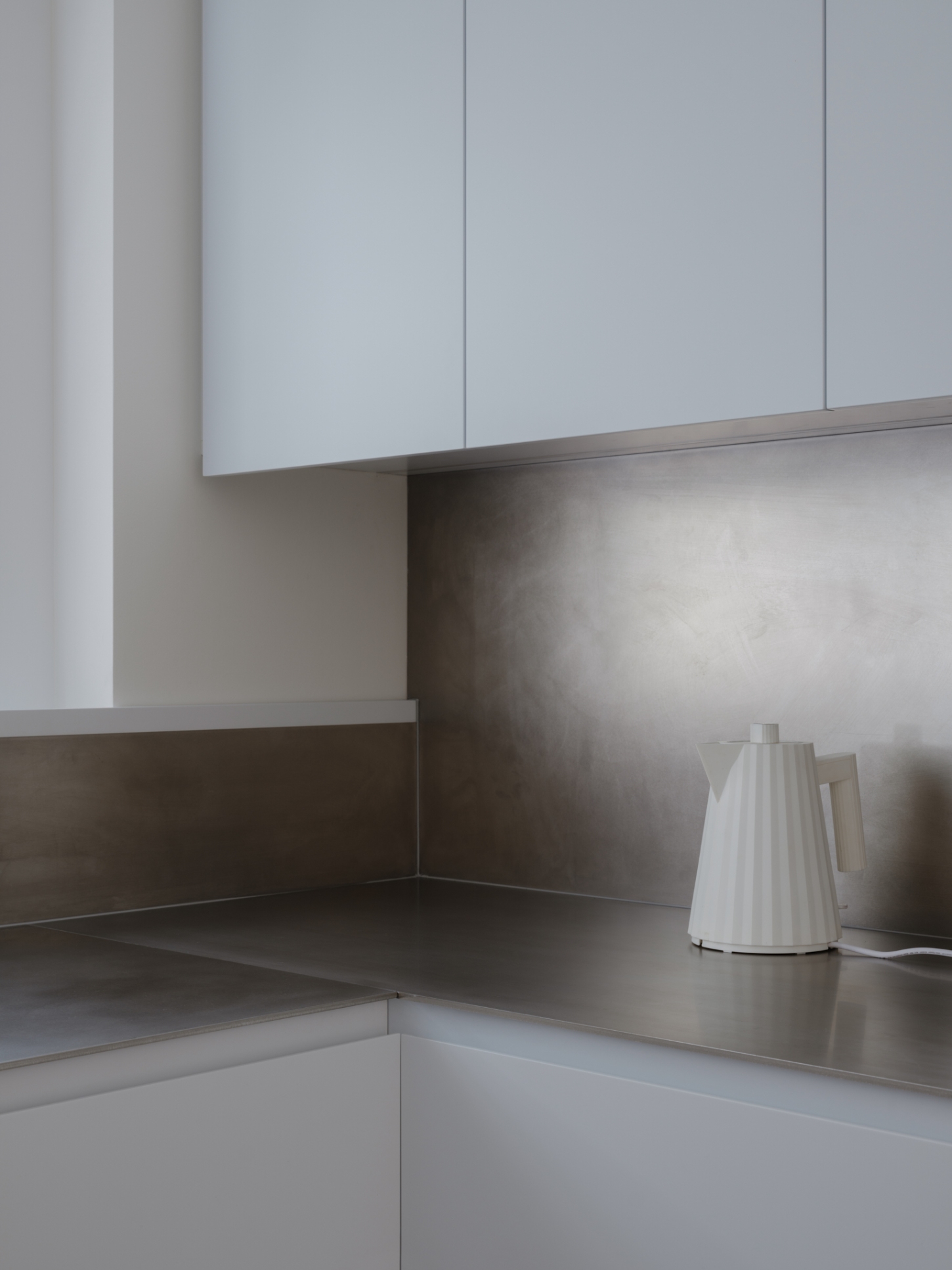 Onslow Gardens Apartment by Youssofzay Hart — A corner kitchen view reveals stainless steel countertops meeting white cabinetry at a right angle.