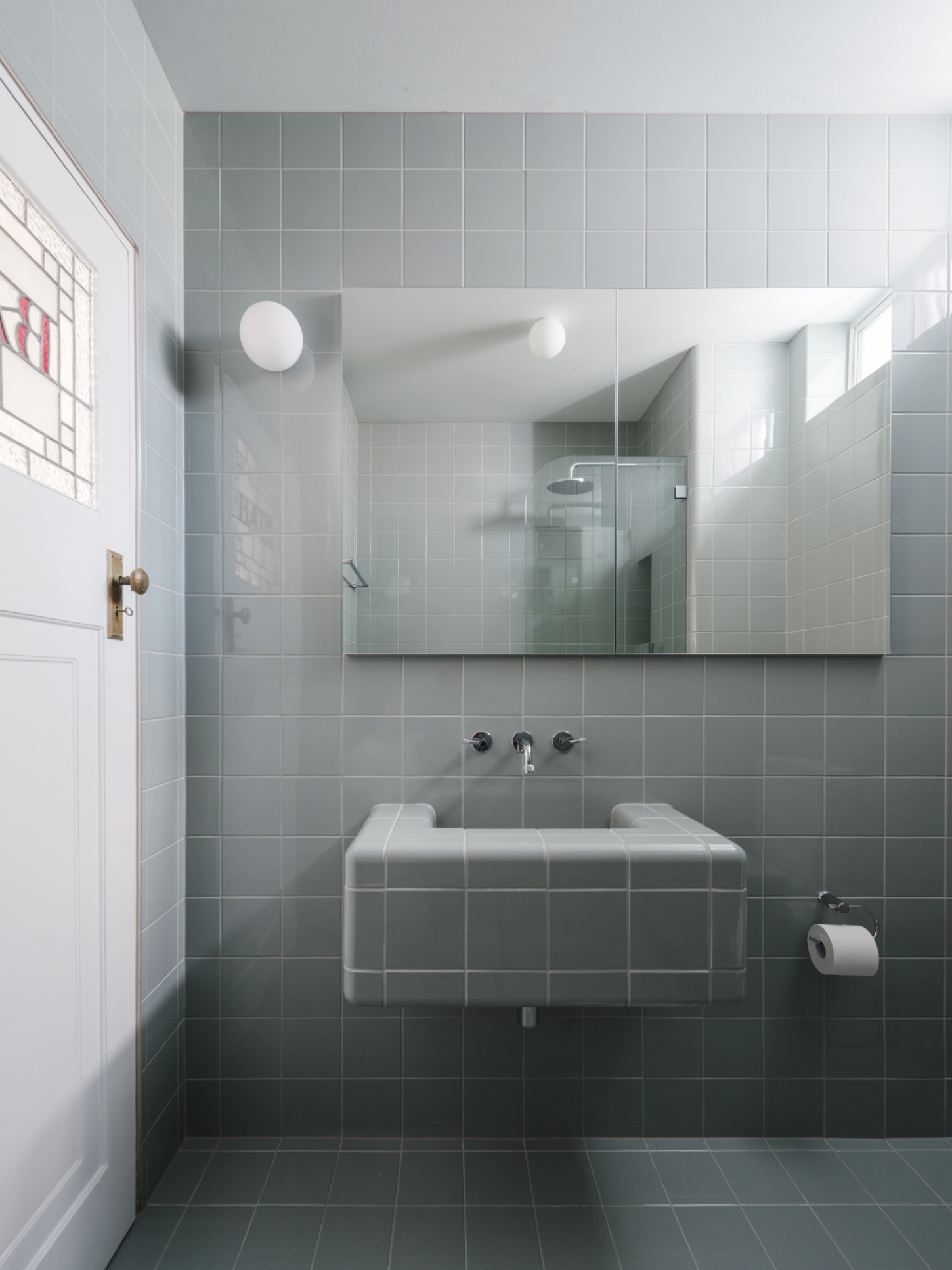 Onslow Gardens Apartment by Youssofzay Hart — The bathroom features a continuous grid of small sage-green ceramic tiles wrapping walls and floor, creating a unified, modular surface.