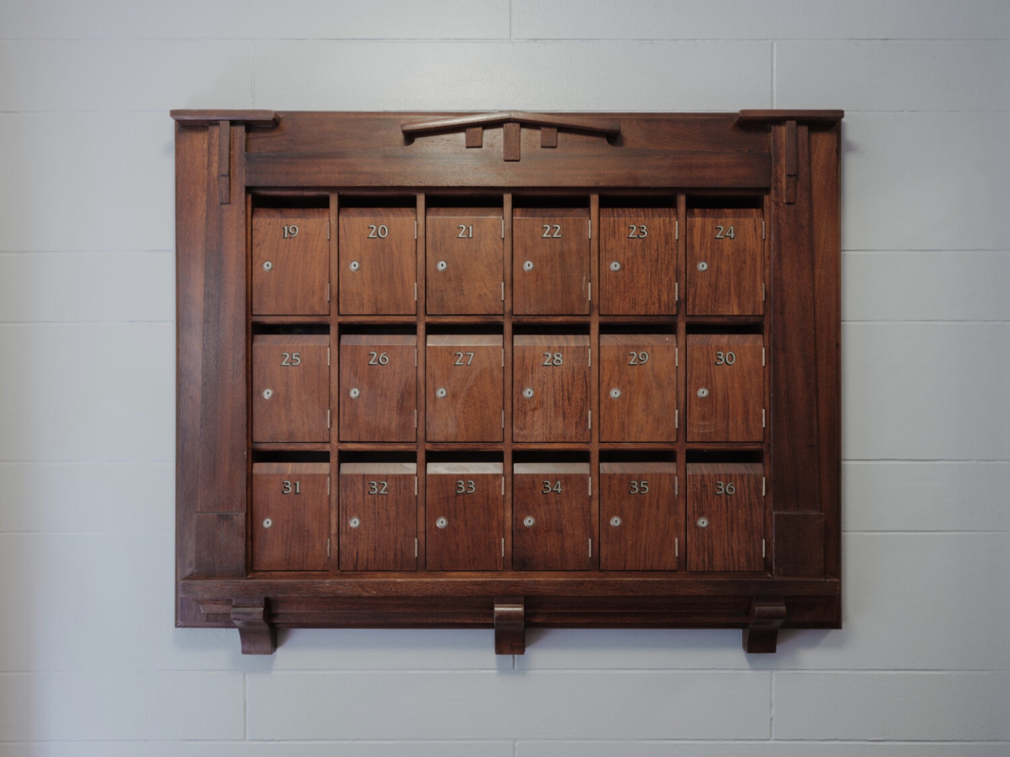 Onslow Gardens Apartment by Youssofzay Hart — A wooden apothecary cabinet with eighteen numbered compartments arranged in three horizontal rows, each drawer marked with brass numerals and fitted with...