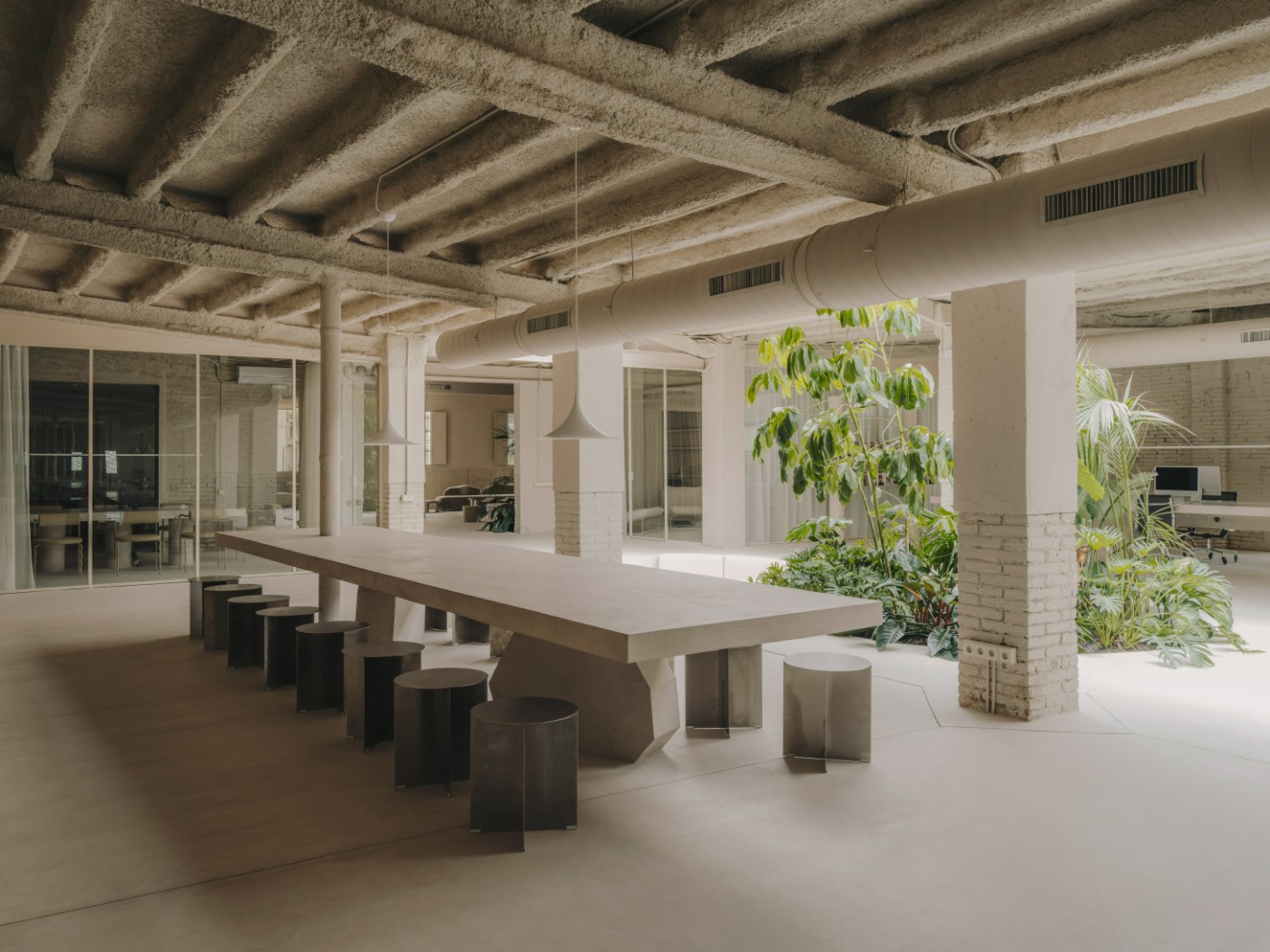 Blow Studio by Isern Serra — A central gathering space anchors this converted warehouse interior, where a monolithic concrete bench curves into a recessed seating pit.