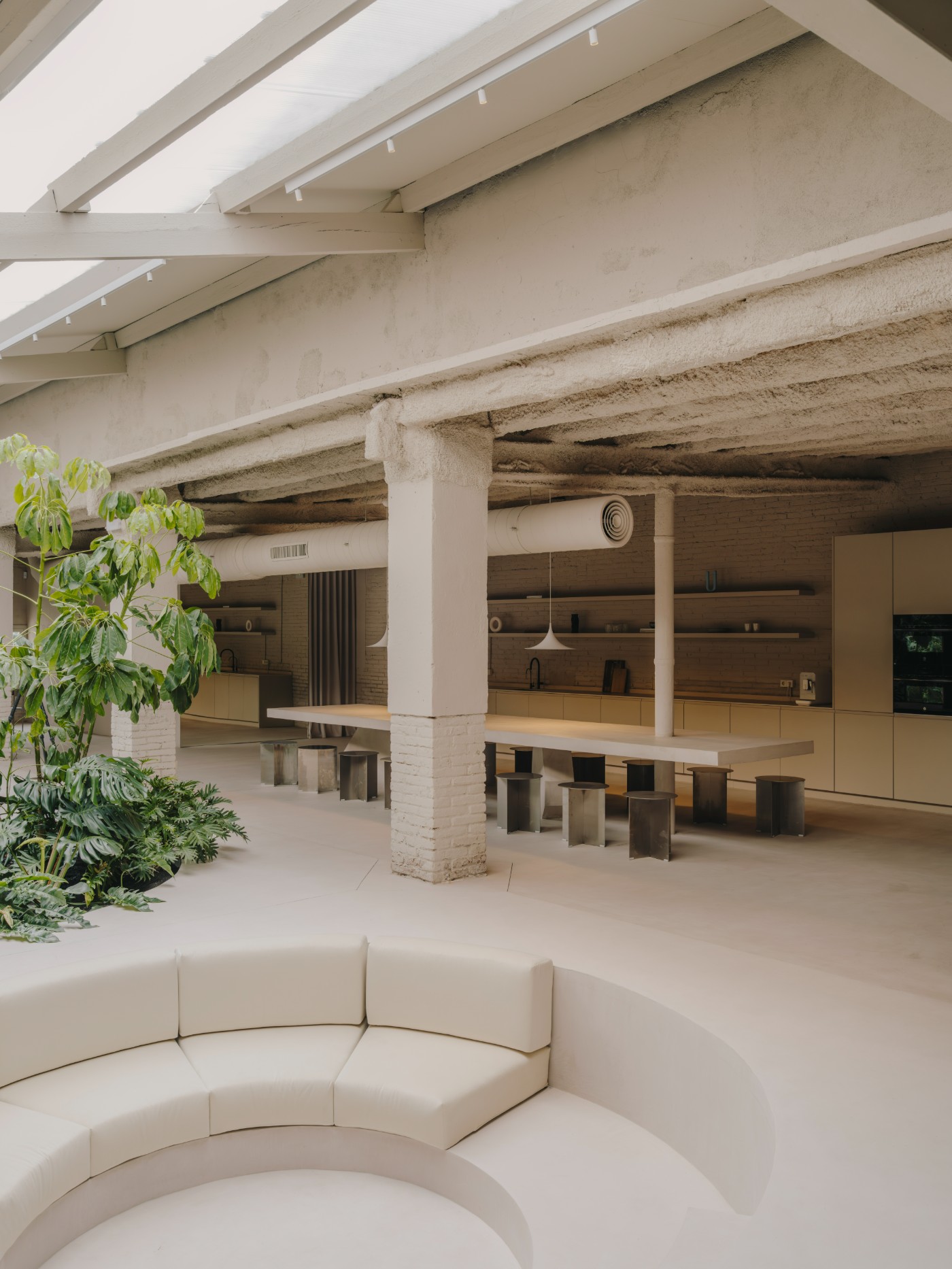 Blow Studio by Isern Serra — The recessed seating pit anchors the foreground, its cream linen upholstery forming continuous curved geometry against the polished concrete floor.