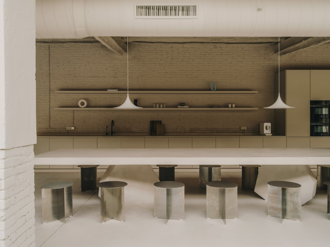 Blow Studio by Isern Serra — Blow Studio's communal hub centers on a recessed circular seating pit carved into polished concrete, its curved edges lined with cream upholstered benches.