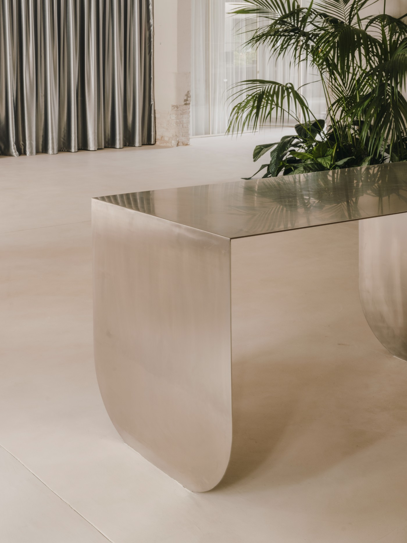 Blow Studio by Isern Serra — A monolithic curved concrete bench wraps around a recessed seating pit, its polished surface reflecting overhead light.