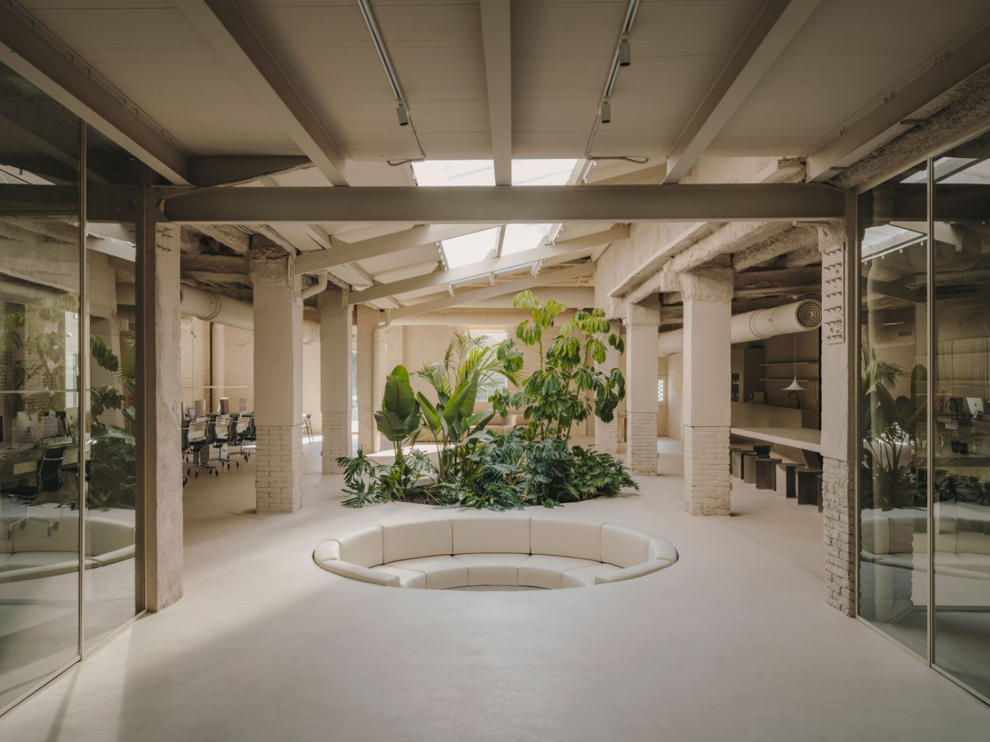 Blow Studio by Isern Serra — A recessed circular seating pit anchors the central volume of this warehouse conversion, its cream-colored upholstered bench following the floor's polished...