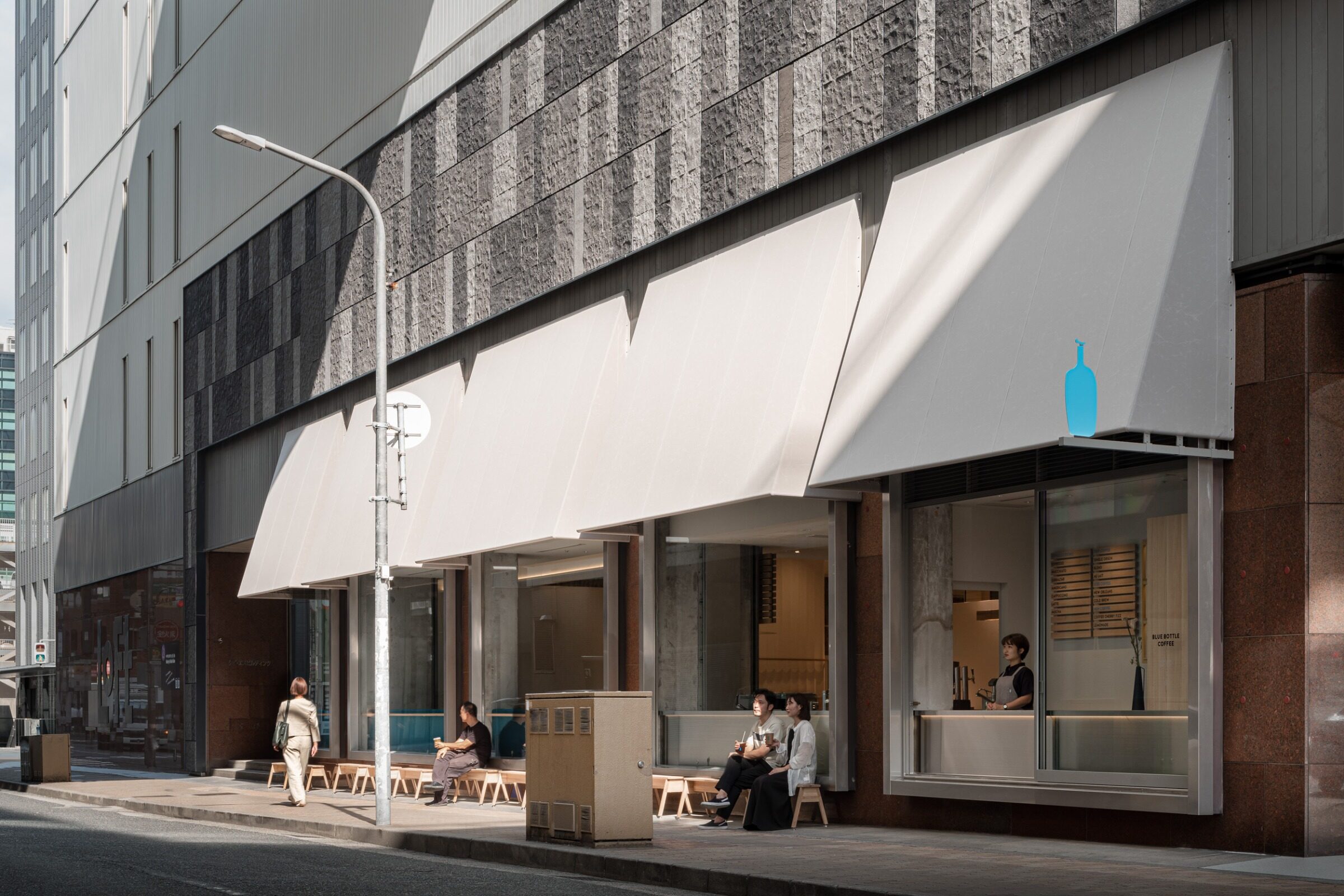 Blue Bottle Coffee Kobe Hankyu Cafe by Keiji Ashizawa — The street-facing elevation of Blue Bottle Coffee's Kobe location presents a composed facade of white canvas awning and glazed storefront.