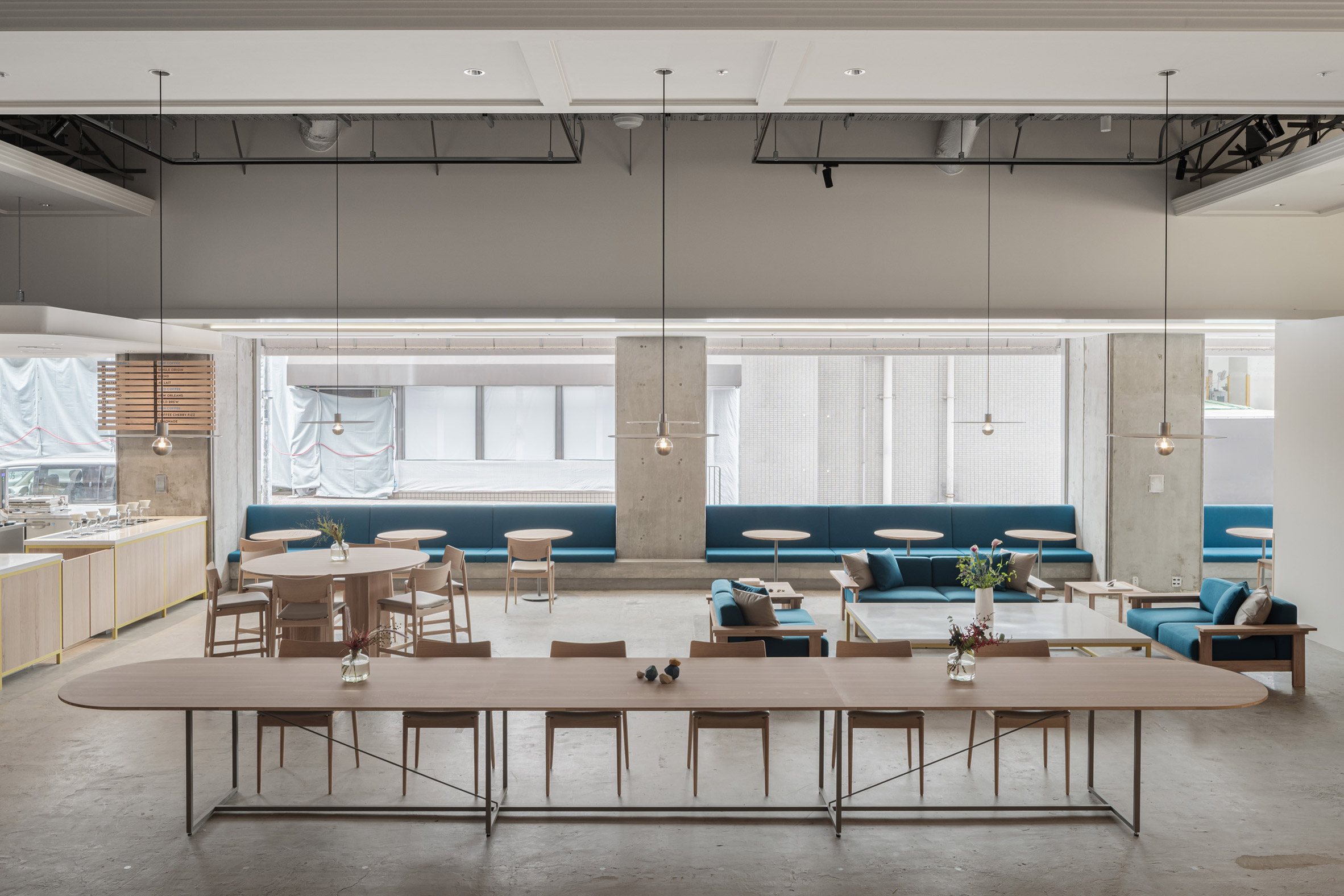Blue Bottle Coffee Kobe Hankyu Cafe by Keiji Ashizawa — The expansive ground floor of Blue Bottle Coffee Kobe Hankyu Cafe presents a horizontally-oriented interior organized around a monumental timber table...