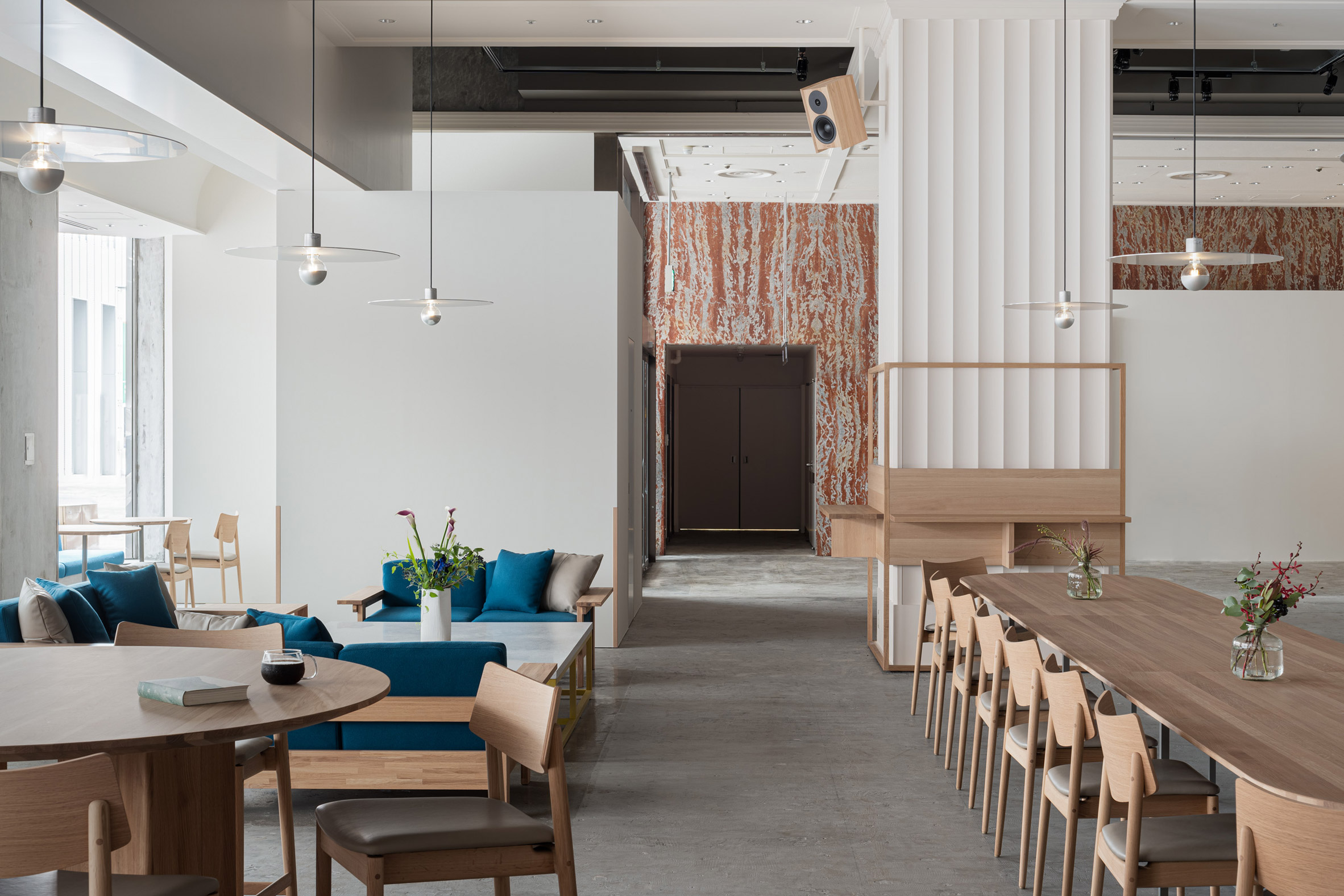 Blue Bottle Coffee Kobe Hankyu Cafe by Keiji Ashizawa — The dining area extends along a timber table with natural wood chairs, anchored by a tall wooden partition with vertical slats that frames the space.