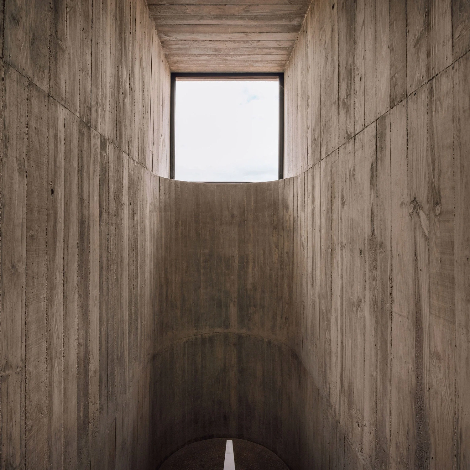 Frame House by Pedro Domingos Arquitectos — A timber-lined concrete passage channels vision toward a rectangular aperture framing pale sky.