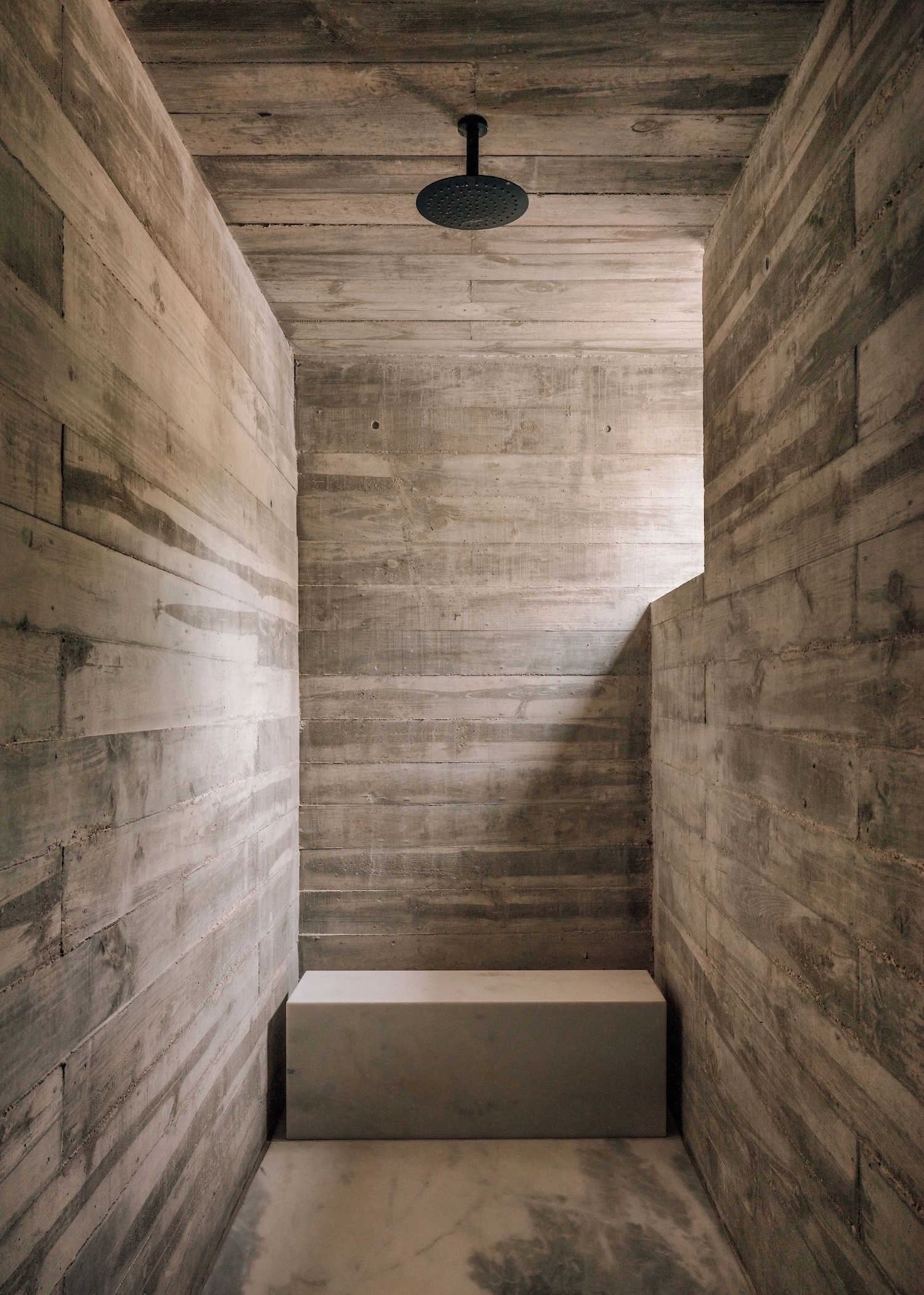 Frame House by Pedro Domingos Arquitectos — A narrow shower enclosure lined with horizontal wood-grain concrete panels, their formwork texture creating rhythmic striations across both side walls and...