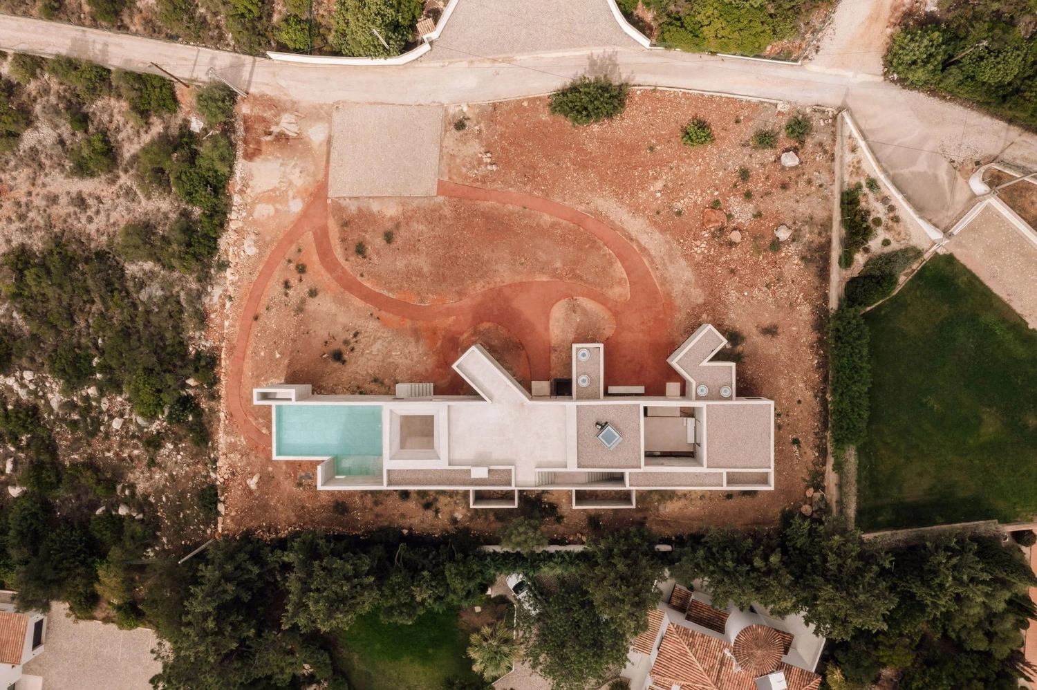 Frame House by Pedro Domingos Arquitectos — Aerial view of Frame House reveals its geometric footprint embedded within terracotta earth and scrubland.