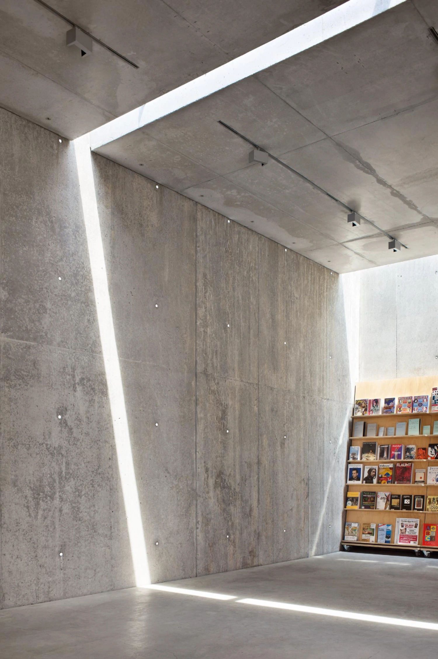 MoMA PS1 Entrance Building by Andrew Berman Architect — The entrance passage is defined by monolithic cast concrete walls bearing the imprint of board formwork, with visible weathering and surface marks creating...