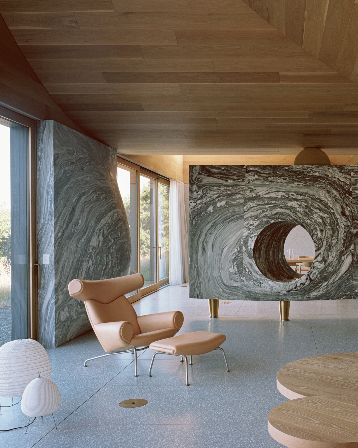 House of Horns by WOJR captured by Nick Dearden — A caramel leather wingback chair with matching ottoman occupies the foreground of this interior, positioned on polished grey terrazzo flooring.