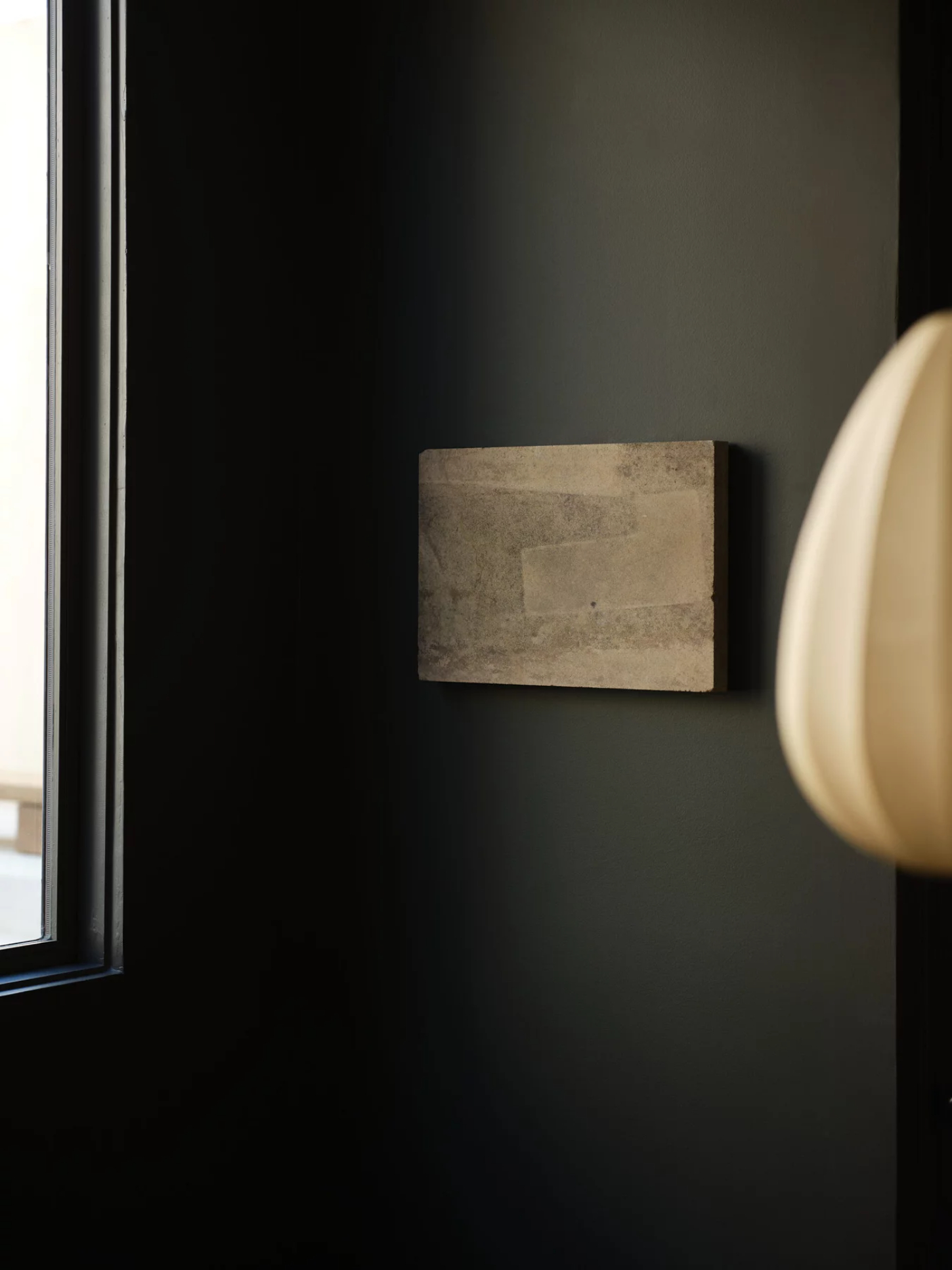 ‘Untitled’ by JAMESPLUMB & Garcé Dimofski at Francis Gallery — A single weathered stone fragment mounted horizontally on a dark wall, its surface marked by distinct tonal variations—pale cream-colored patches indicating...