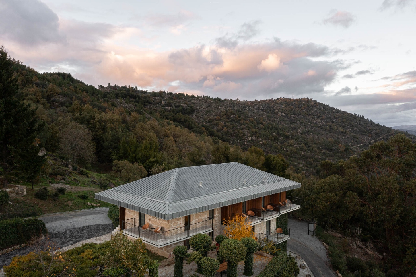 The Vagar Country House by David Bilo and Filipe Pina — A single-story country house photographed at golden hour, its corrugated metal roof with central ridge beam dominating the composition.