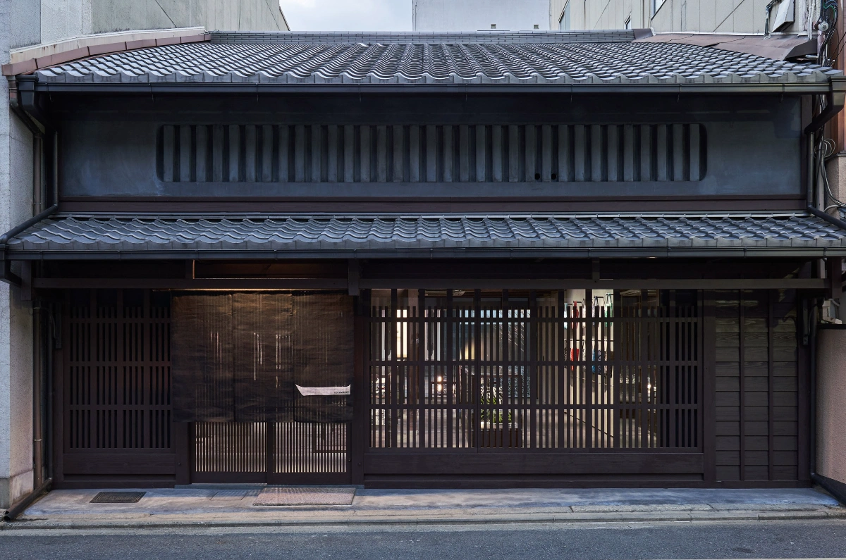 Issey Miyake Kyoto by Naoto Fukasawa Design — The storefront elevation of the Issey Miyake Kyoto flagship reveals a recessed facade composed of vertical timber lattice screens in dark charcoal, creating...