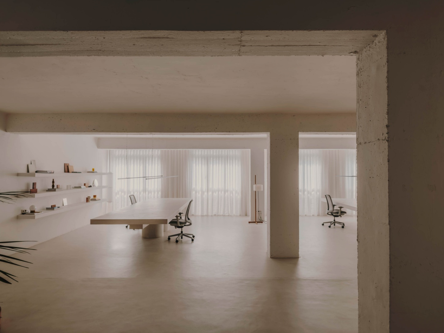 Isern Serra Studio — A 200-square-meter studio interior anchored by a cantilevered timber desk with visible shadow gap beneath, positioned off-center in the whitewashed concrete...