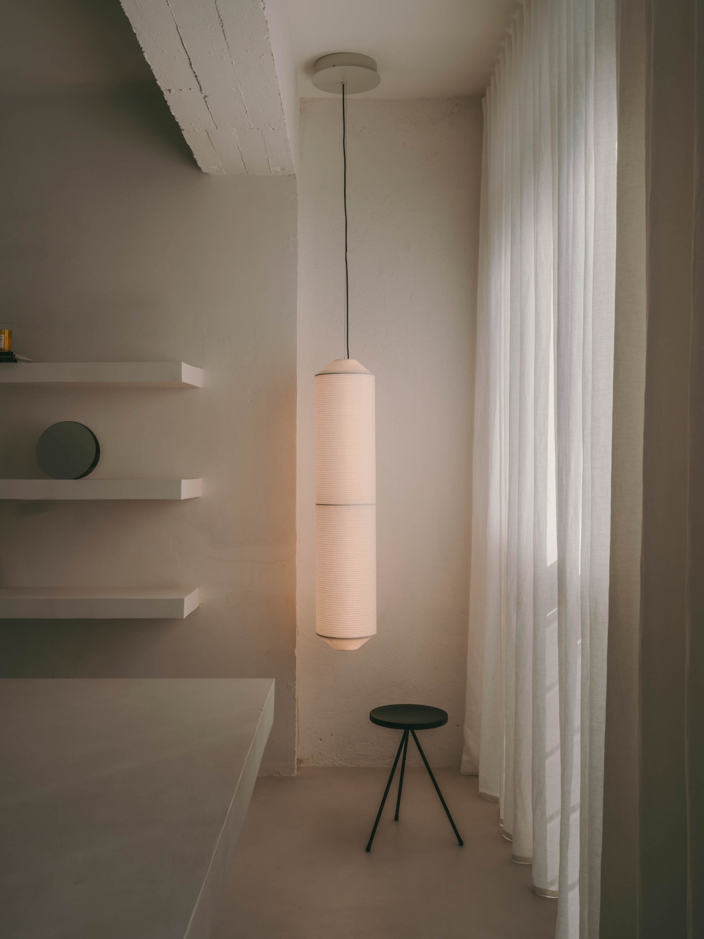 Isern Serra Studio — A pendant light suspended from the ceiling defines the narrow passage, its cylindrical ribbed fabric shade glowing warmly against whitewashed walls.