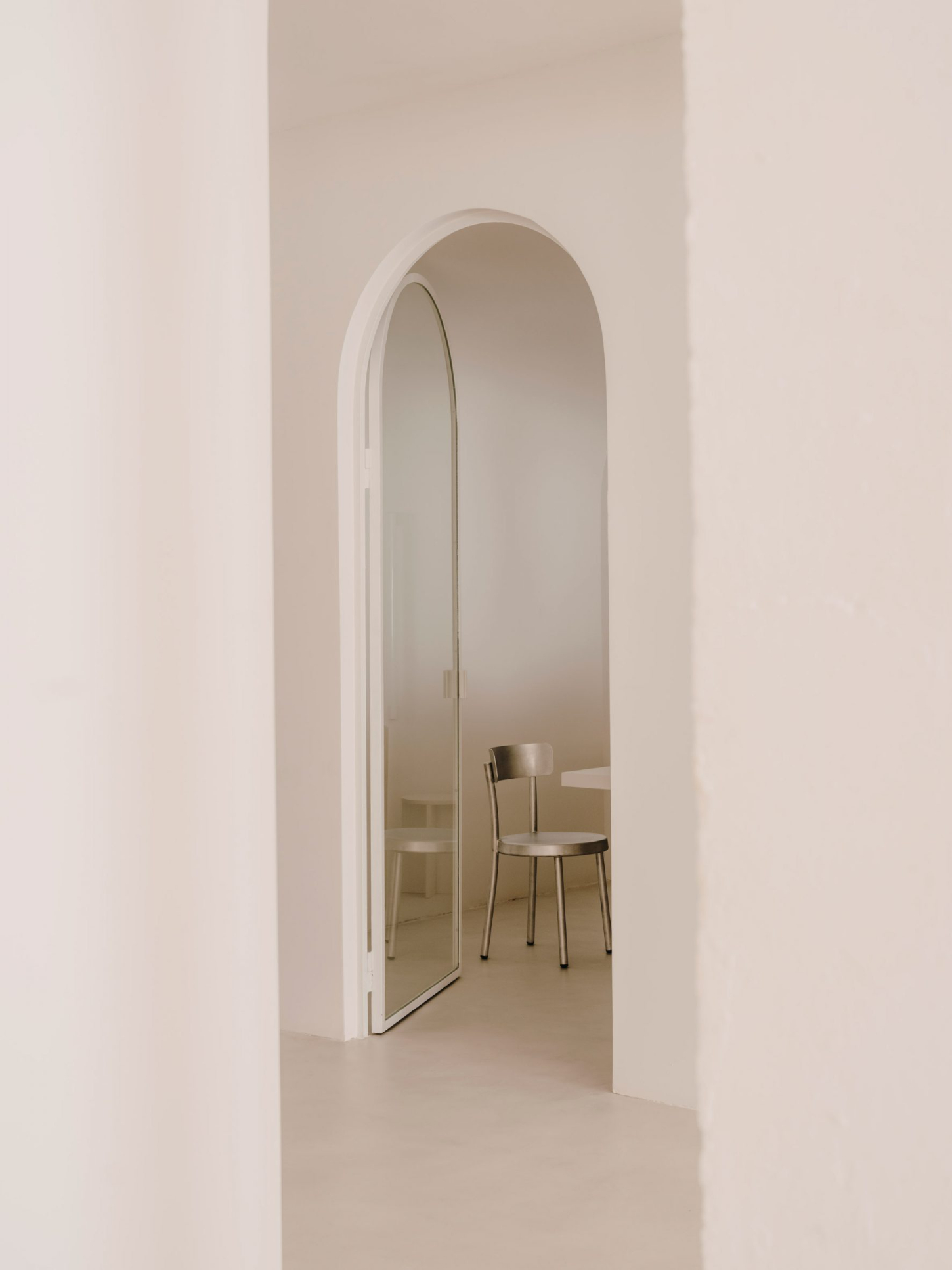 Isern Serra Studio — An arched passageway frames a monochromatic interior where whitewashed plaster walls meet polished concrete flooring.