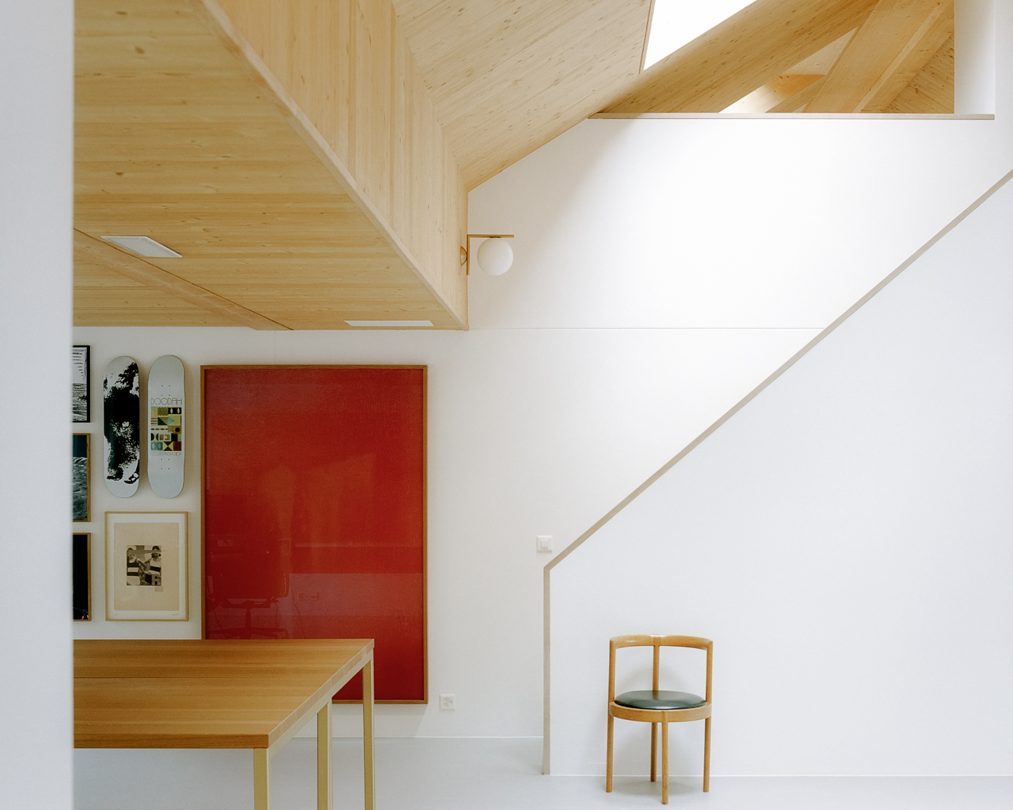 Yves Suter Atelier — A double-height atelier space defined by exposed pine beam geometry and zenithal skylights that cast linear shadows across white plaster walls.