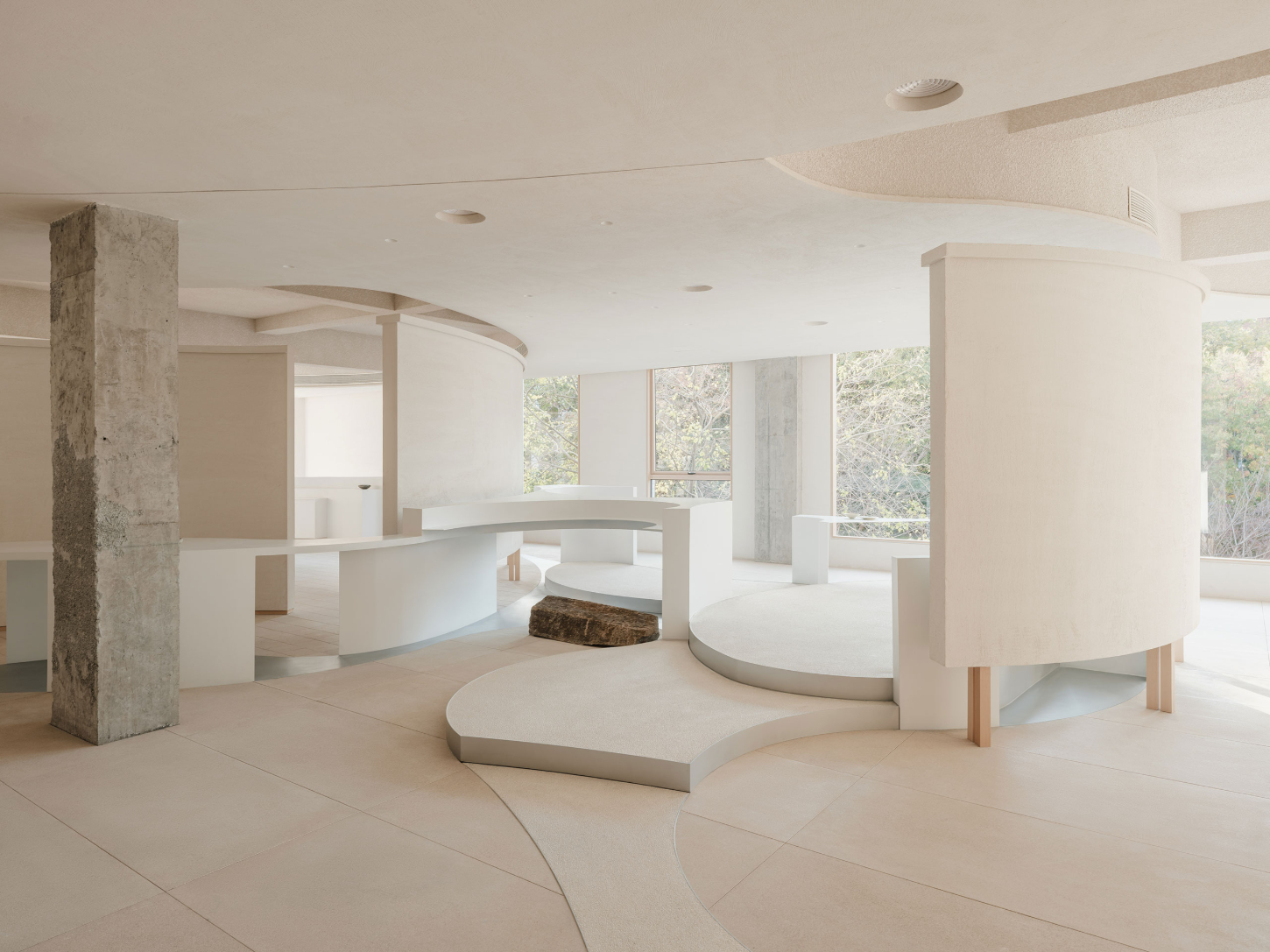JIA Garden by Mountain Soil — The showroom interior presents a sculptural arrangement of white curved platforms and rammed-earth structural columns set against cream tile flooring.