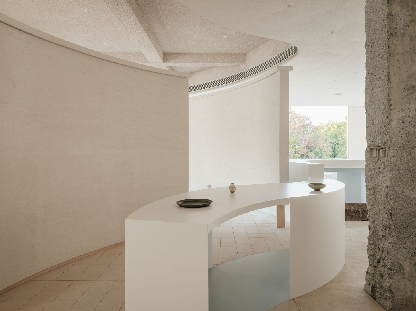 JIA Garden by Mountain Soil — A curved white display counter dominates the showroom, its organic form creating a threshold between viewing zones.