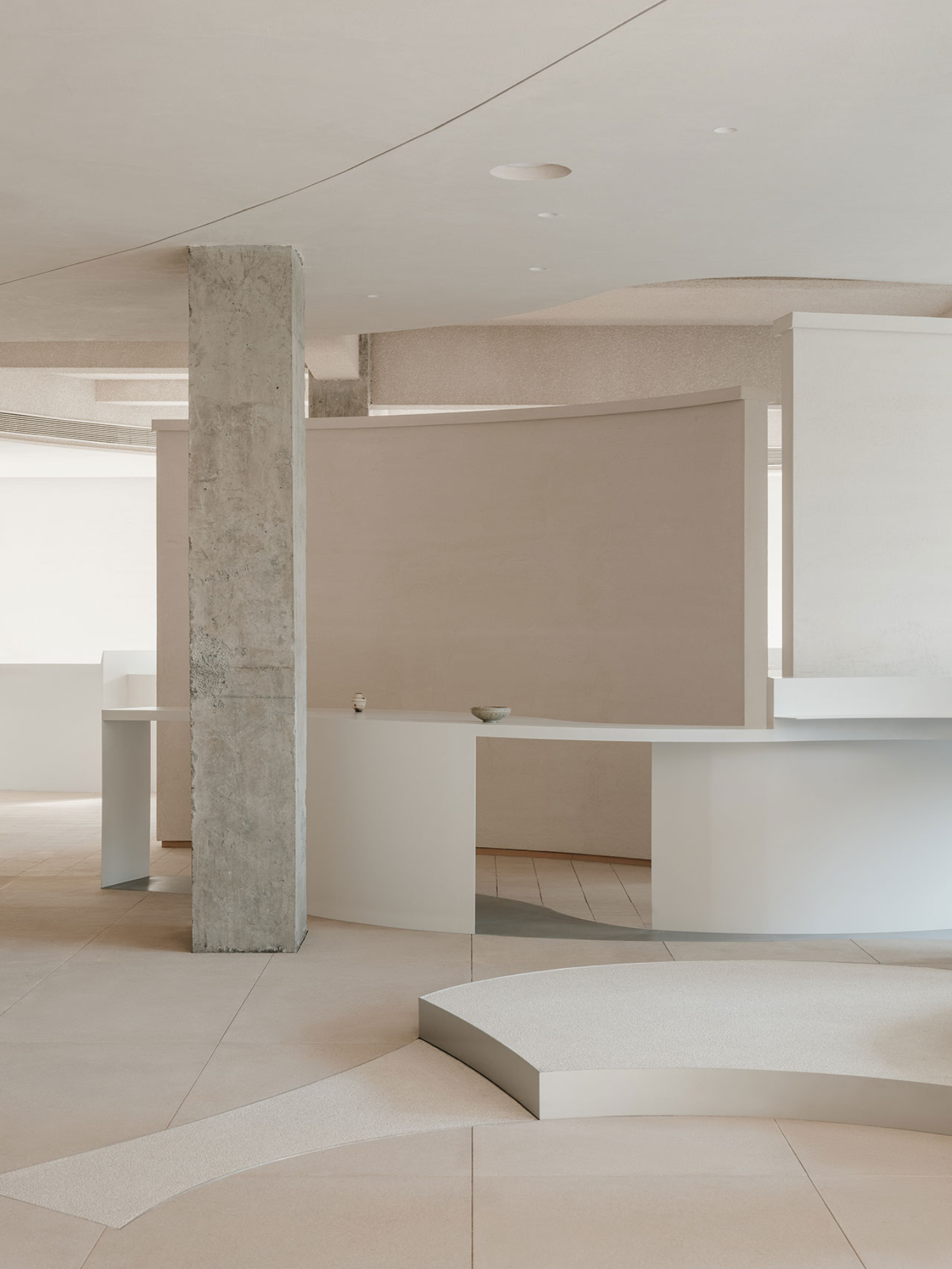 JIA Garden by Mountain Soil — A minimalist retail interior featuring a curved white display counter and organic-form table anchoring the foreground, with deliberately spaced ceramic...