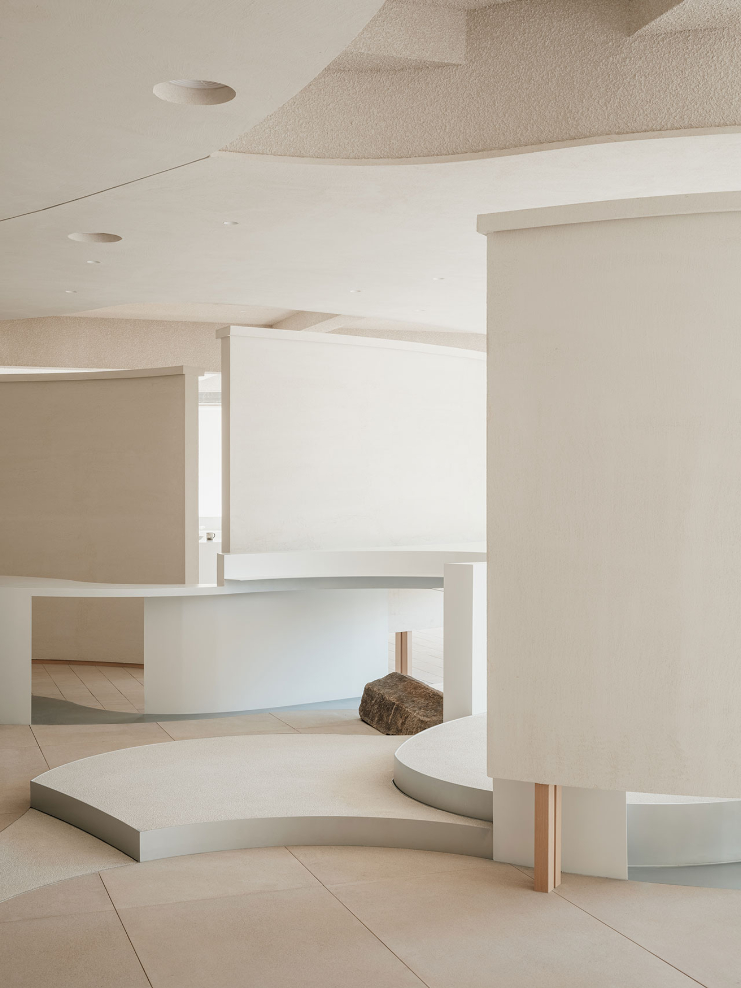 JIA Garden by Mountain Soil — The JIA Garden showroom presents a minimalist retail environment composed of curved white platforms and recessed display surfaces set against cream-rendered...
