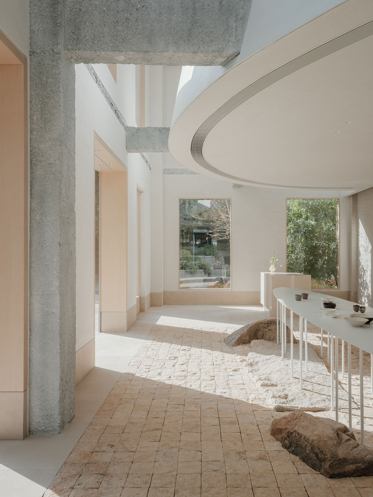 JIA Garden by Mountain Soil — A minimalist interior space featuring a white elongated display table with deliberate ceramic vessel arrangements in cream, dark brown, and white.