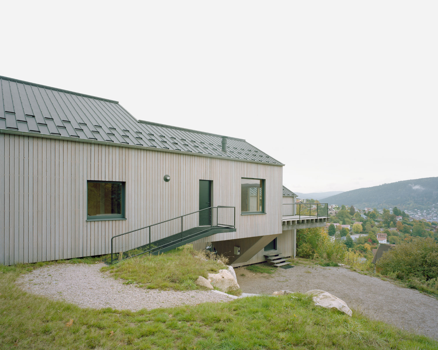 Maison Hiltiti captured by Rasmus Norlander by Atelier Ordinaire — Maison Hiltiti presents a corrugated metal-clad exterior elevated on a concrete base, with a sloped green metal roof punctuated by rectangular windows and a...