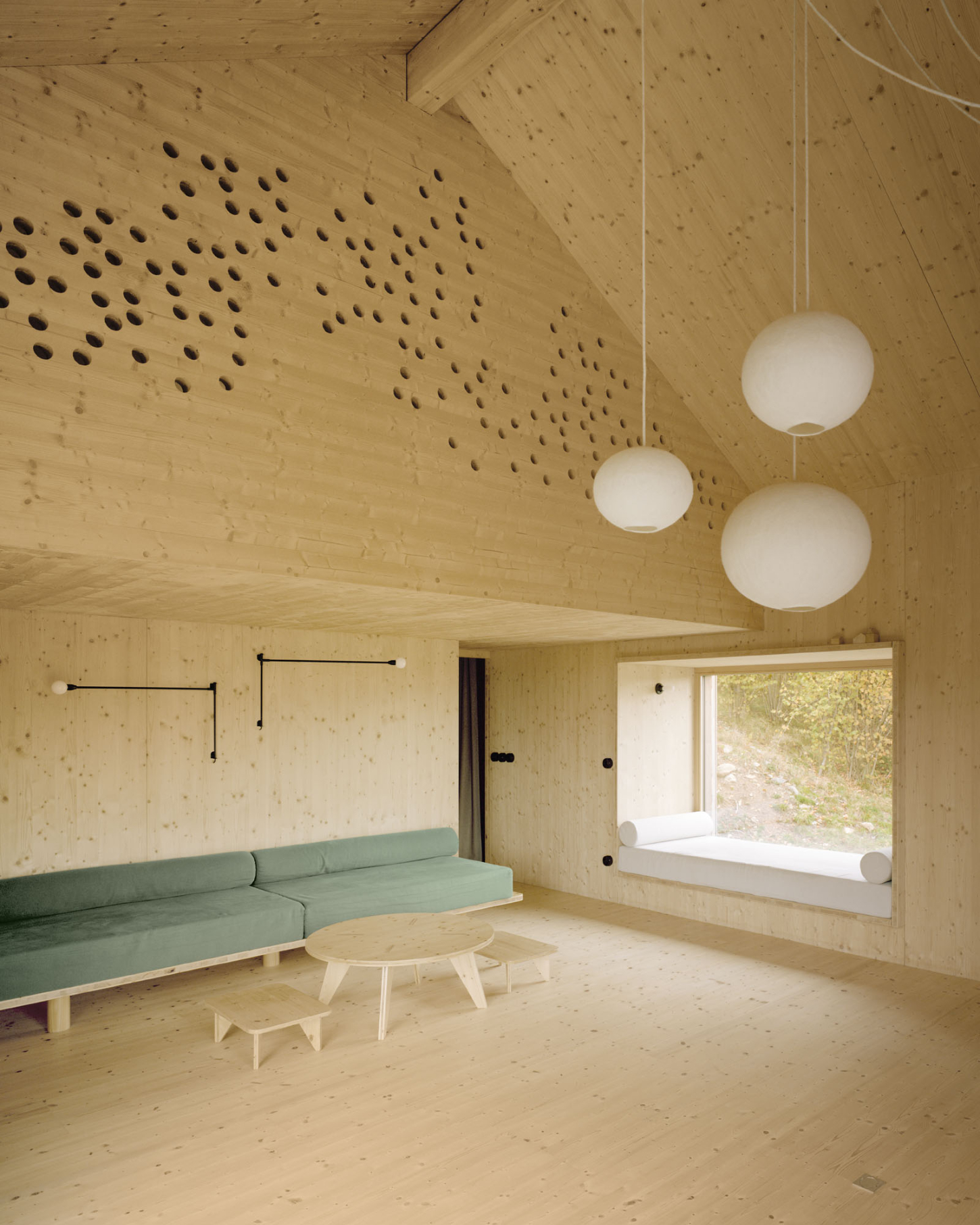 Maison Hiltiti captured by Rasmus Norlander by Atelier Ordinaire — A timber-lined interior showcases cross-laminated wood construction across walls and ceiling, punctuated by a grid of regularly spaced circular perforations.