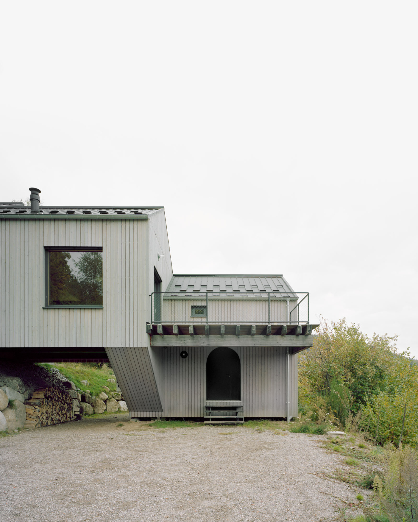 Maison Hiltiti captured by Rasmus Norlander by Atelier Ordinaire — Maison Hiltiti presents a modular timber structure elevated on a gravel forecourt, its corrugated metal cladding painted in pale grey-green tones.