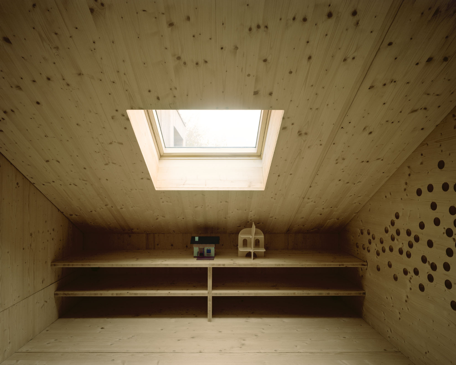 Maison Hiltiti captured by Rasmus Norlander by Atelier Ordinaire — A timber-lined attic interior with cross-laminated wood ceiling and walls punctuated by regularly-spaced circular knotholes.
