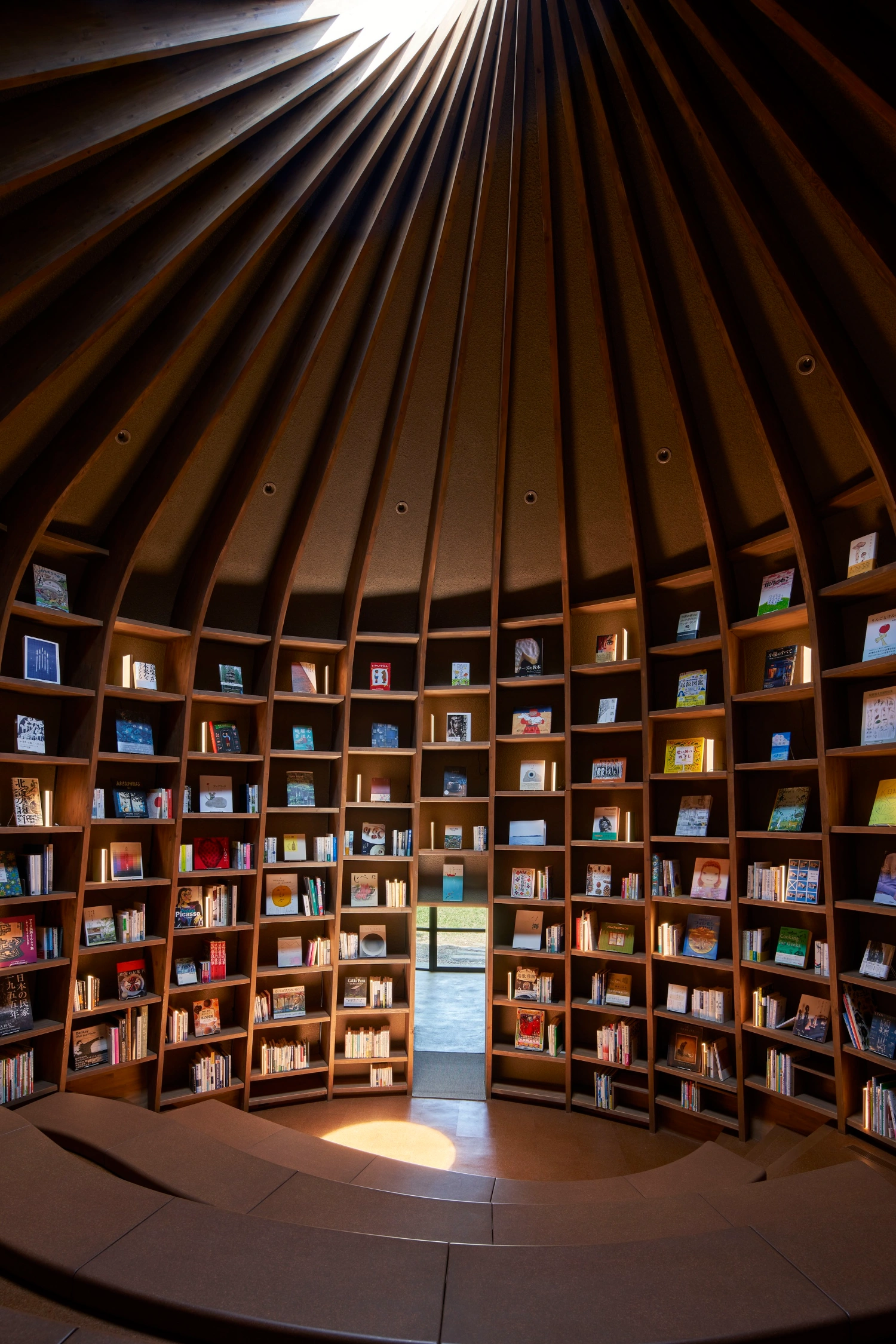 Library in the Earth by Hiroshi Nakamura & NAP — Interior view of a domed timber library with radial ribbed wooden structure ascending to a skylit apex.