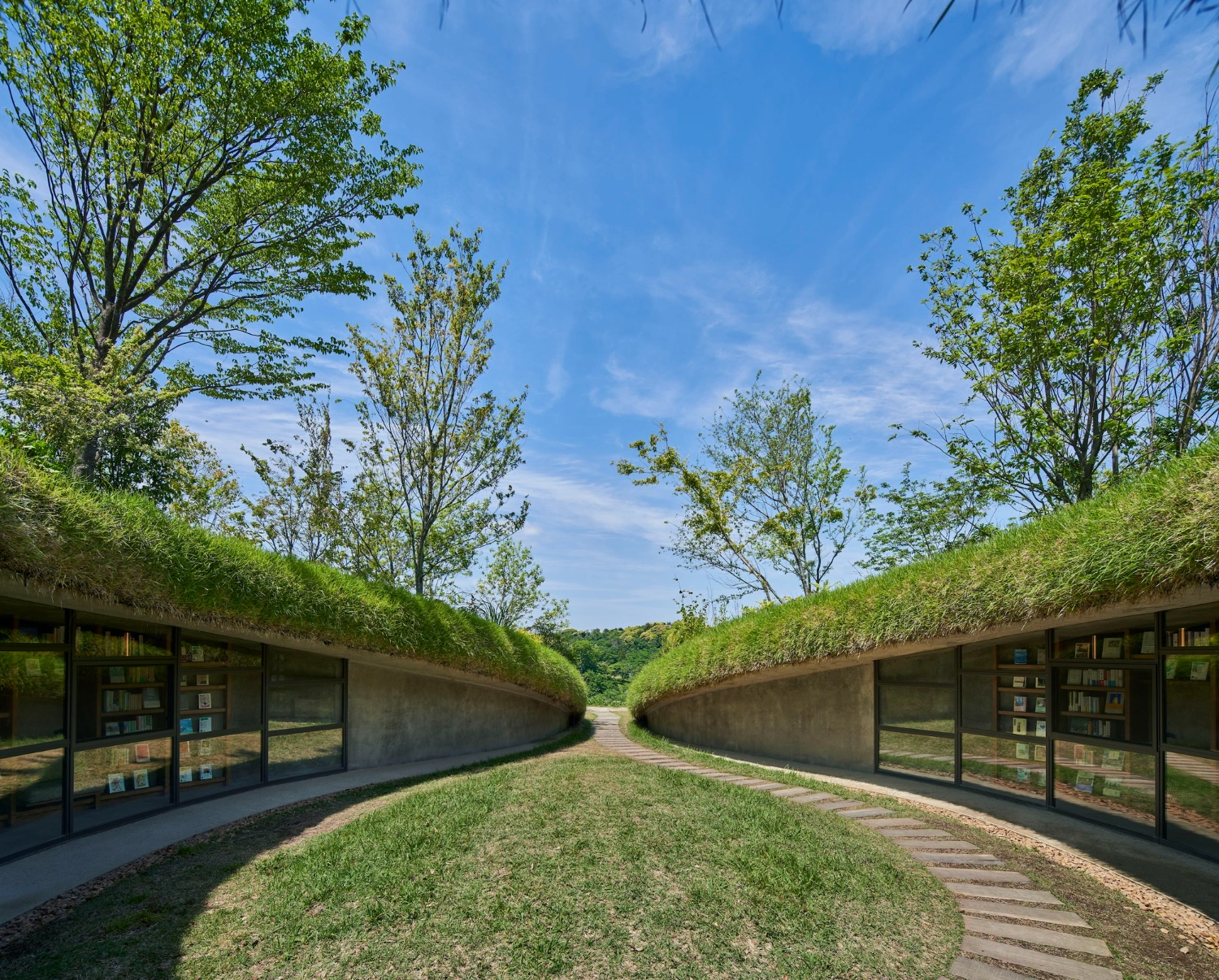 Library in the Earth by Hiroshi Nakamura & NAP — A symmetrical passage carved into an earthen berm, with dark concrete or timber-clad structures flanking both sides.