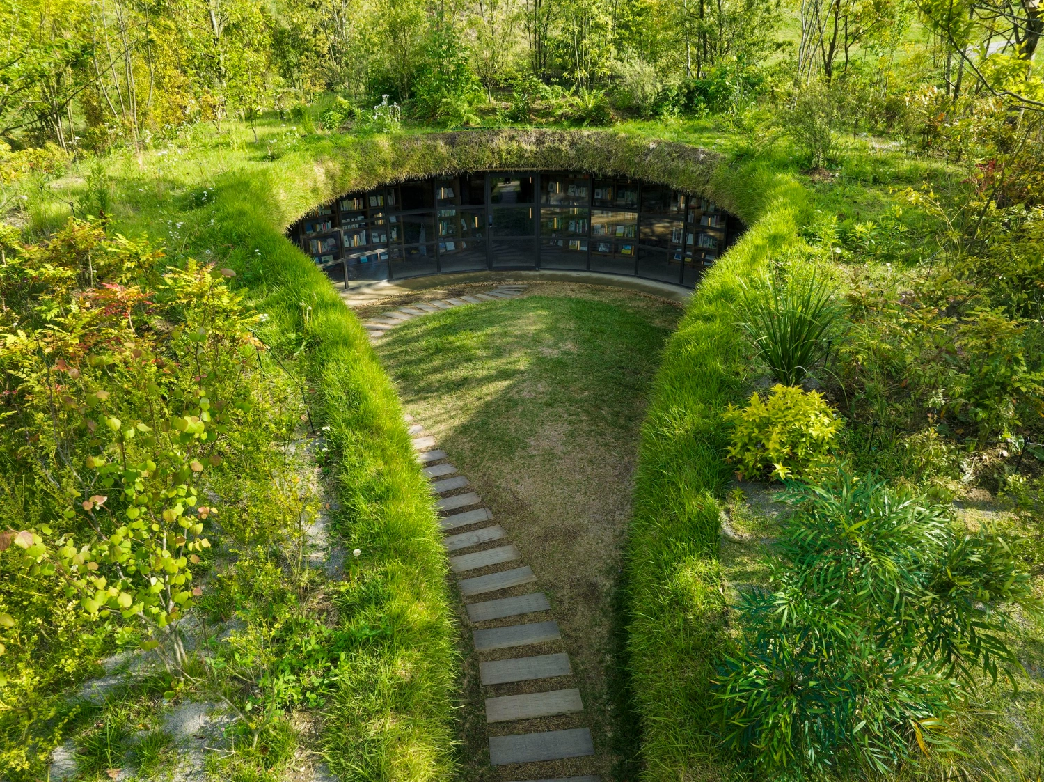 Library in the Earth by Hiroshi Nakamura & NAP — A recessed library entrance framed by a pathway of stepping stones descending into an earthen berm.