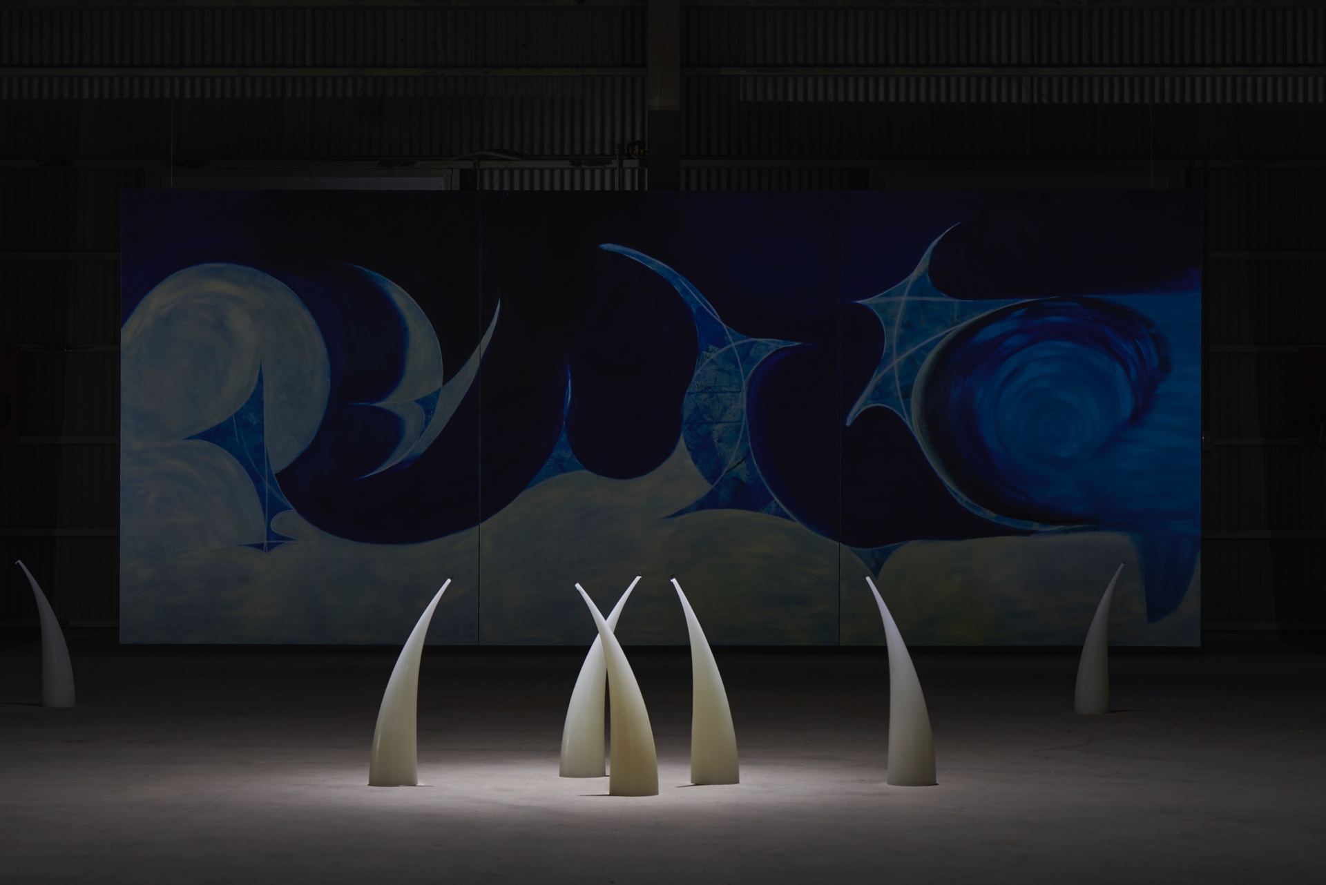 Like seeing this world for the first time by Kenji Sakai — Five tapering cream-colored cone forms, evenly spaced across a polished concrete floor, occupy the foreground of an abandoned factory gallery.