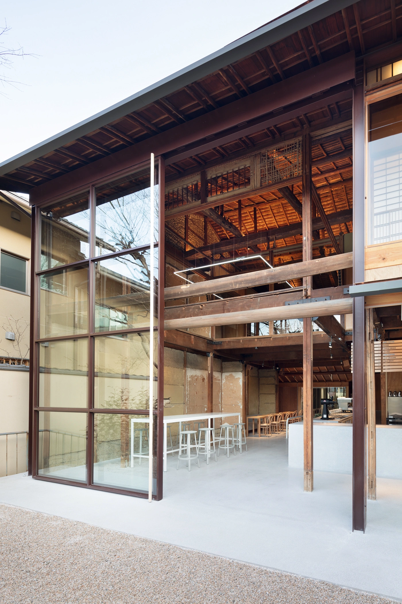 Blue Bottle Coffee Kyoto Cafe by Schemata Architects — The café's threshold dissolves architectural boundaries through a full-height glass sliding door system that frames the interior counter and white bar seating.