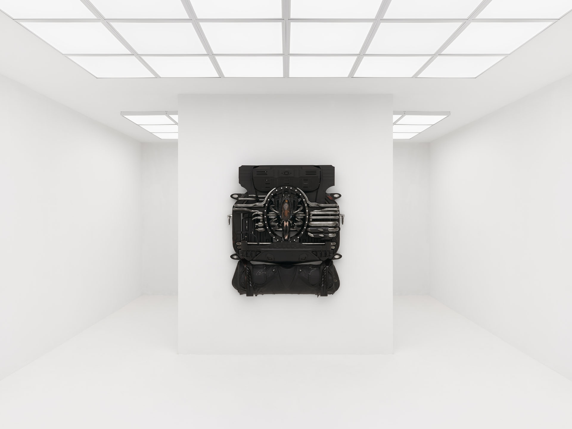 ENDO– by Taylor Ashby Hawkins at ASHES/ASHES — A wall-mounted sculpture presents disassembled automotive engine components—ribbed aluminum cylinder heads and finned cooling structures—arranged...