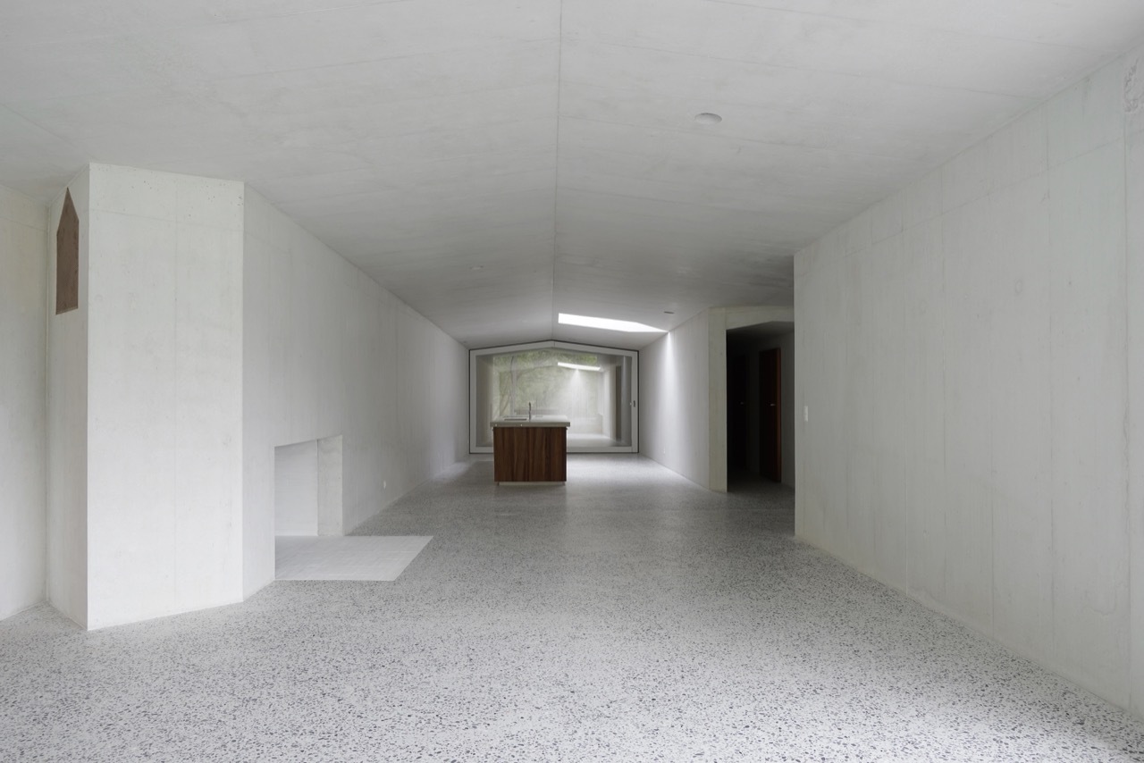 House in Laax by Valerio Olgiati — Interior view of a single-story residential space with monolithic white concrete walls and a polished aggregate concrete floor.