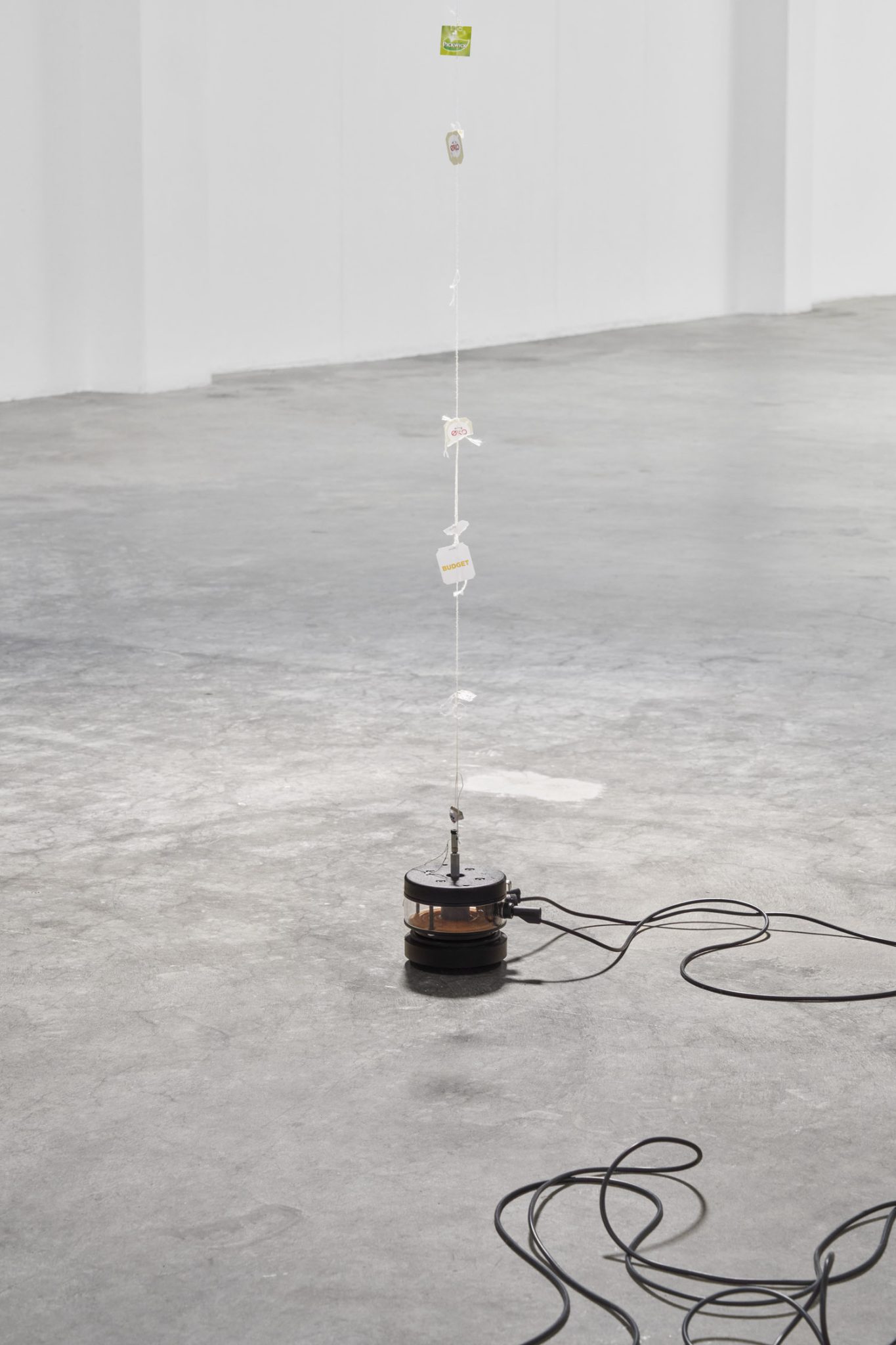 Future Mechanism Rag Plus Two Grams by Nina Canell at Simian — A vertical installation anchors the gallery floor: a black cylindrical motor or mechanical base connects via coiled electrical cord to a thin vertical wire...