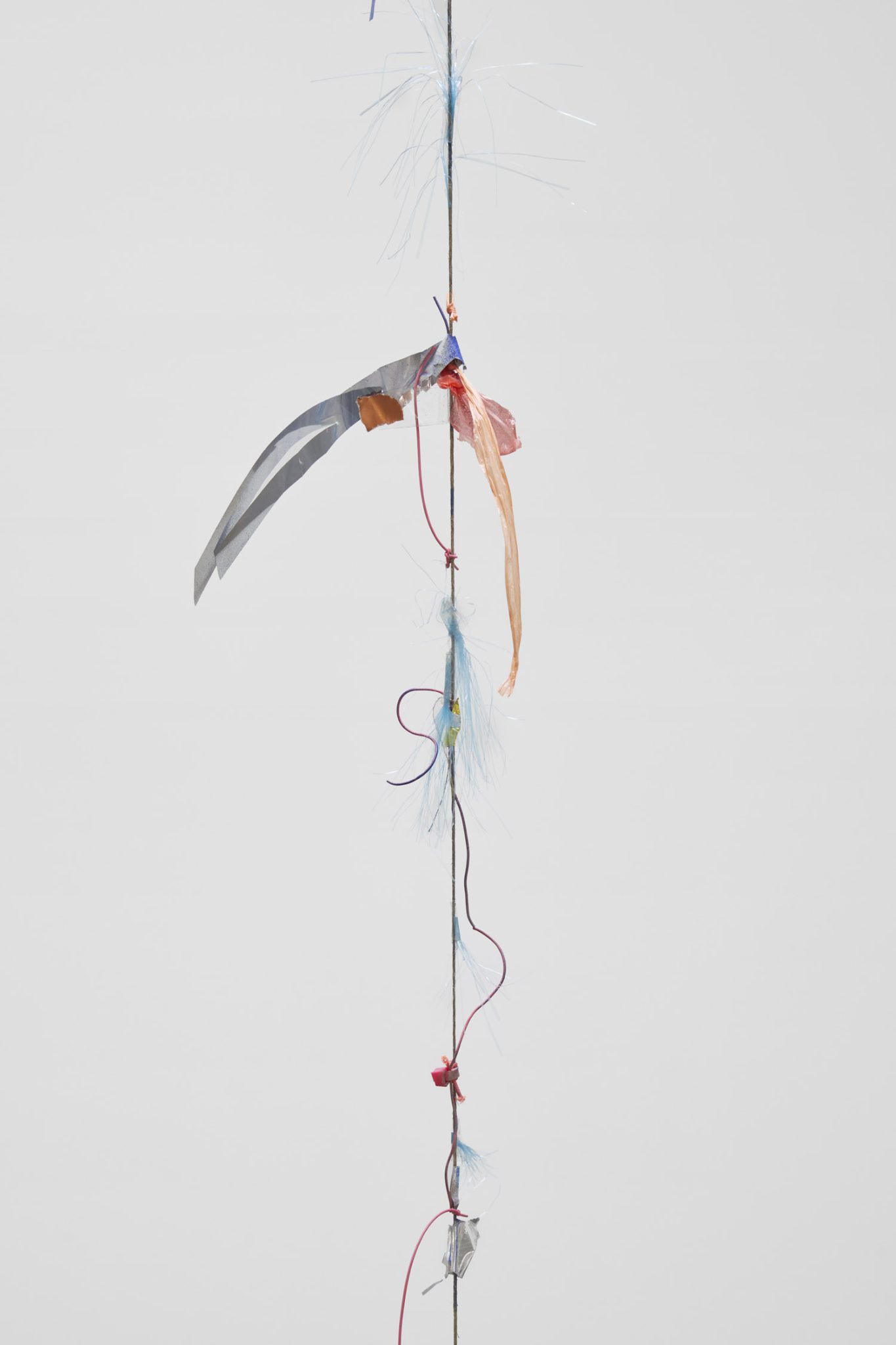 Future Mechanism Rag Plus Two Grams by Nina Canell at Simian — A vertical fiber optic or light-conducting filament is suspended against a neutral ground, anchored by a dark central line.