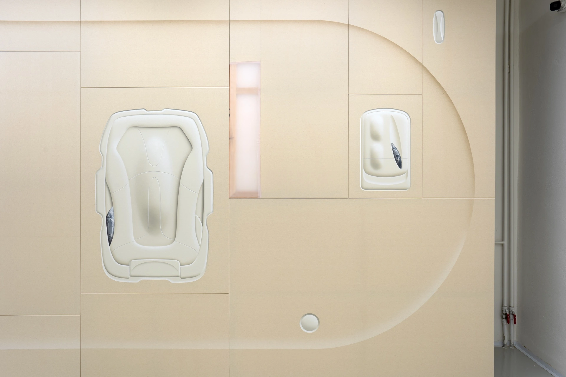 [face_not_recognized] by Milan Vagač — A cream-colored, tile-clad wall features two recessed openings containing white molded forms: a larger rectangular cavity on the left holds an abstracted...