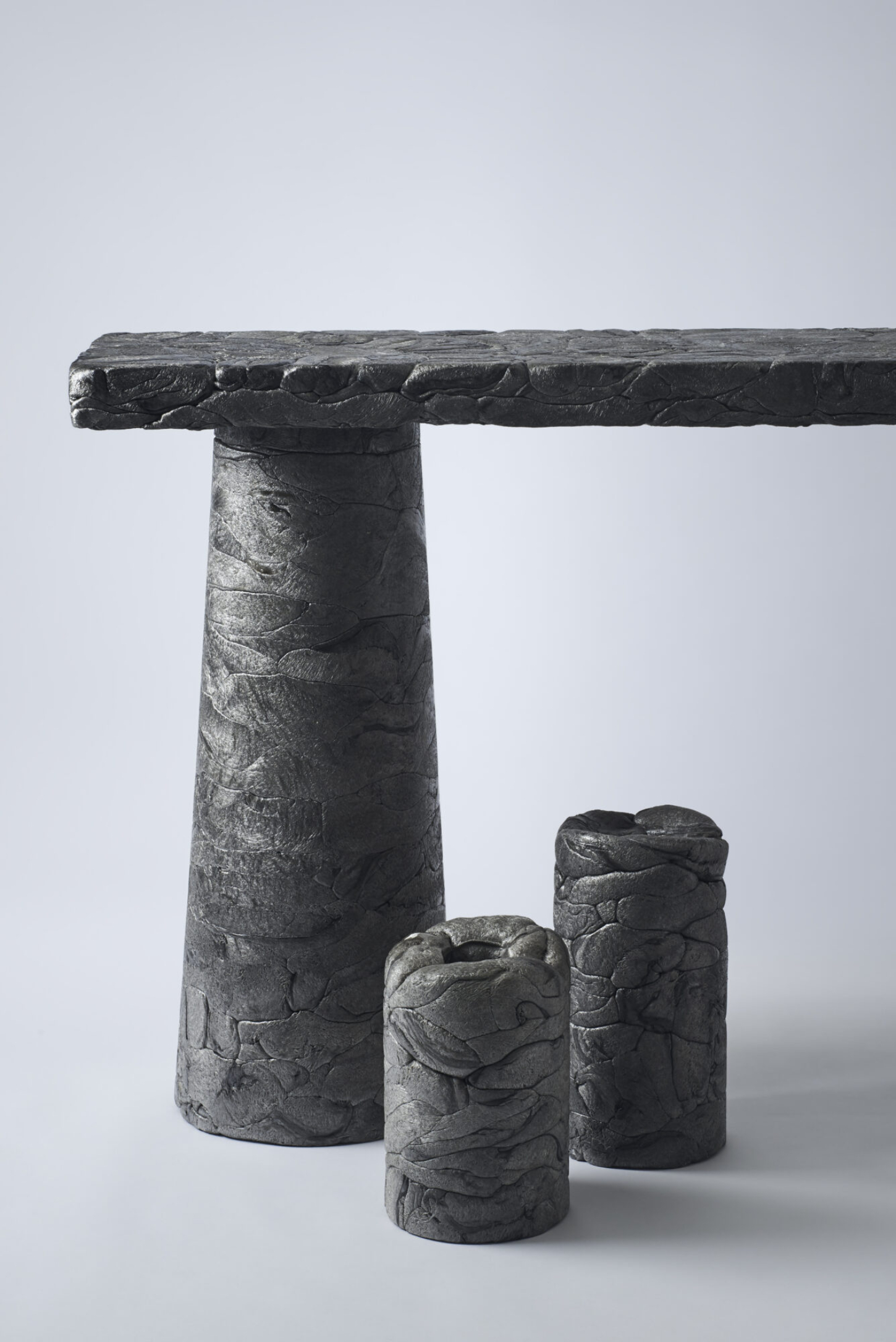 Refoam by We+ — A sculptural table object in cast concrete composed of three cylindrical supports beneath a horizontal beam.