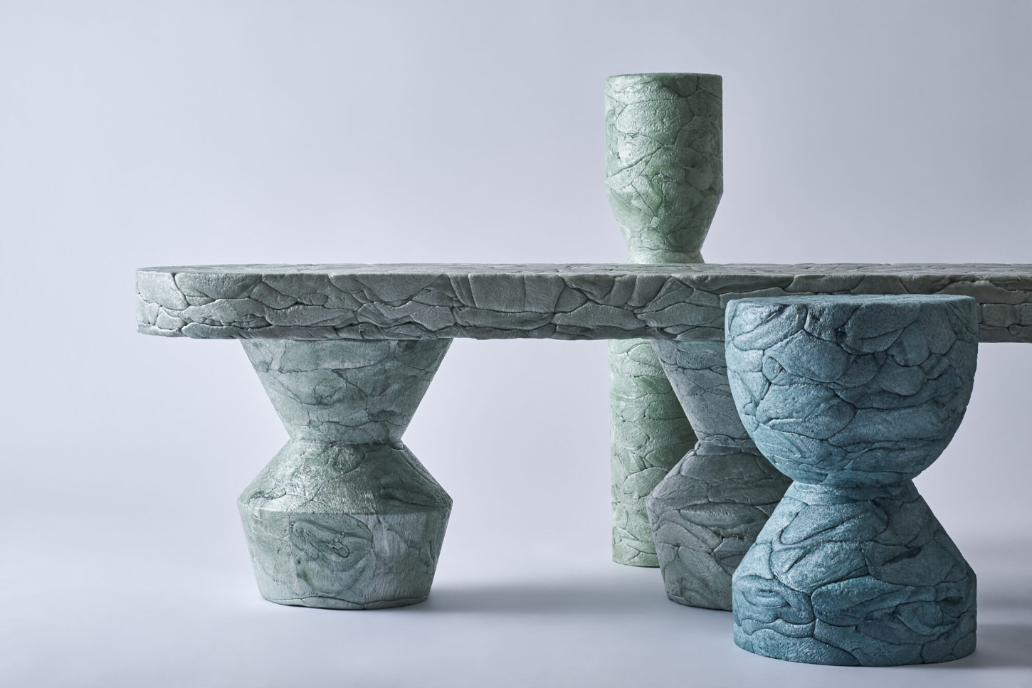 Refoam by We+ — A sculptural bench system composed of cast concrete or stone elements featuring deeply carved leaf and scale motifs across all surfaces.