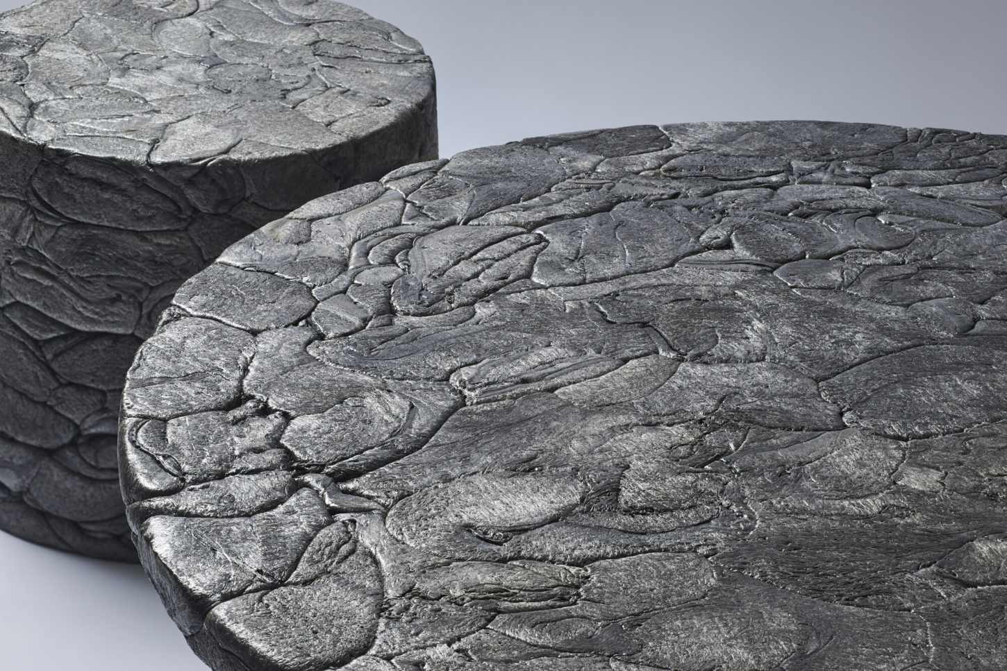 Refoam by We+ — A cylindrical concrete capital carved with overlapping acanthus-leaf or scale motifs in high relief, photographed in close-up detail.