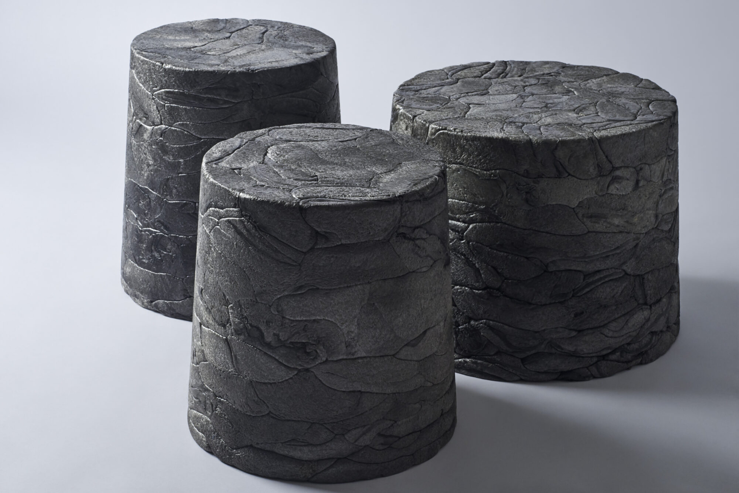 Refoam by We+ — Three cylindrical vessels arranged in graduated heights, their surfaces densely carved with overlapping acanthus or scale-like leaf motifs.