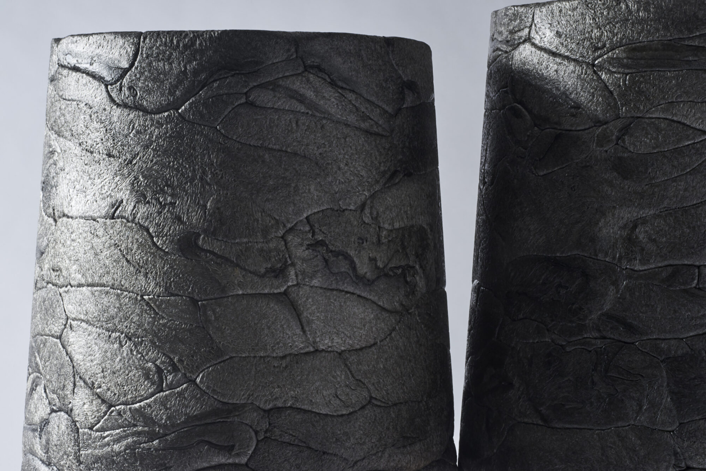 Refoam by We+ — Close-up detail of a cylindrical architectural element carved with overlapping leaf or scale motifs arranged in vertical registers.