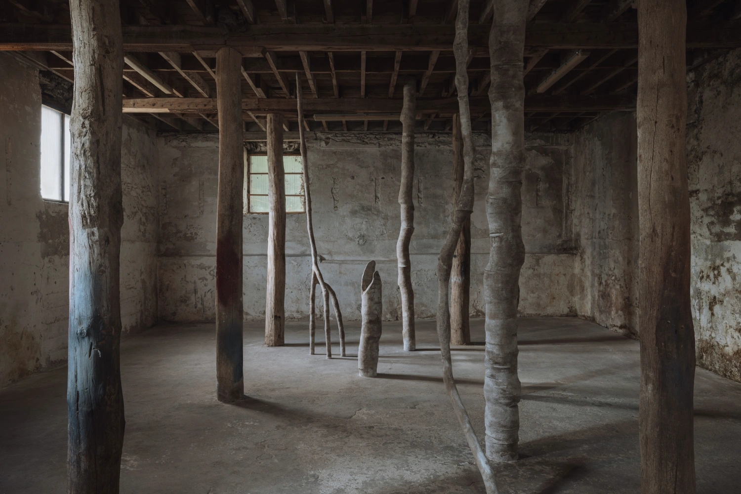 remember member ember by Carolina Aguirre at THE MILL — Three columnar concrete forms with organically bifurcating upper sections occupy a raw concrete floor within an industrial interior space.